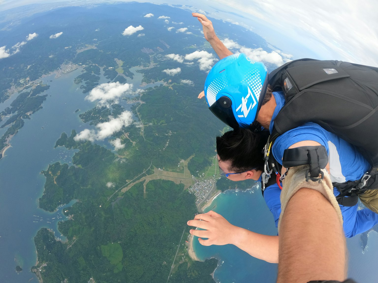 Due persone che si divertono in caduta libera durante un salto in paracadute con isole verdi e oceano blu sullo sfondo