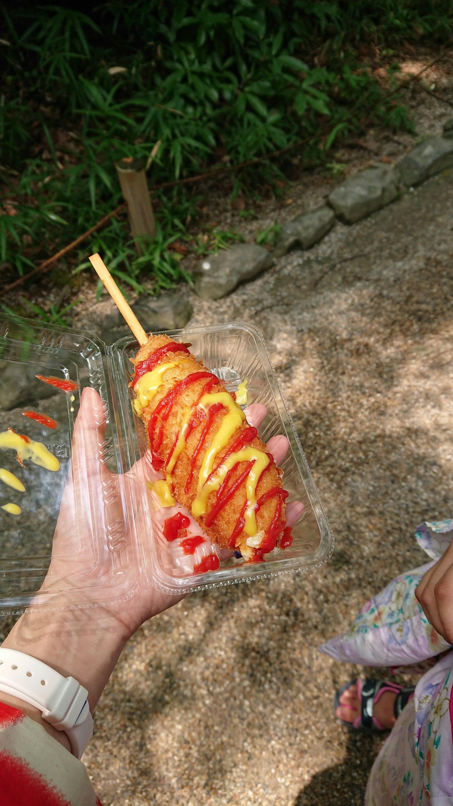 Hot-dog coloré tenu dans une main avec du ketchup et de la moutarde sur le dessus