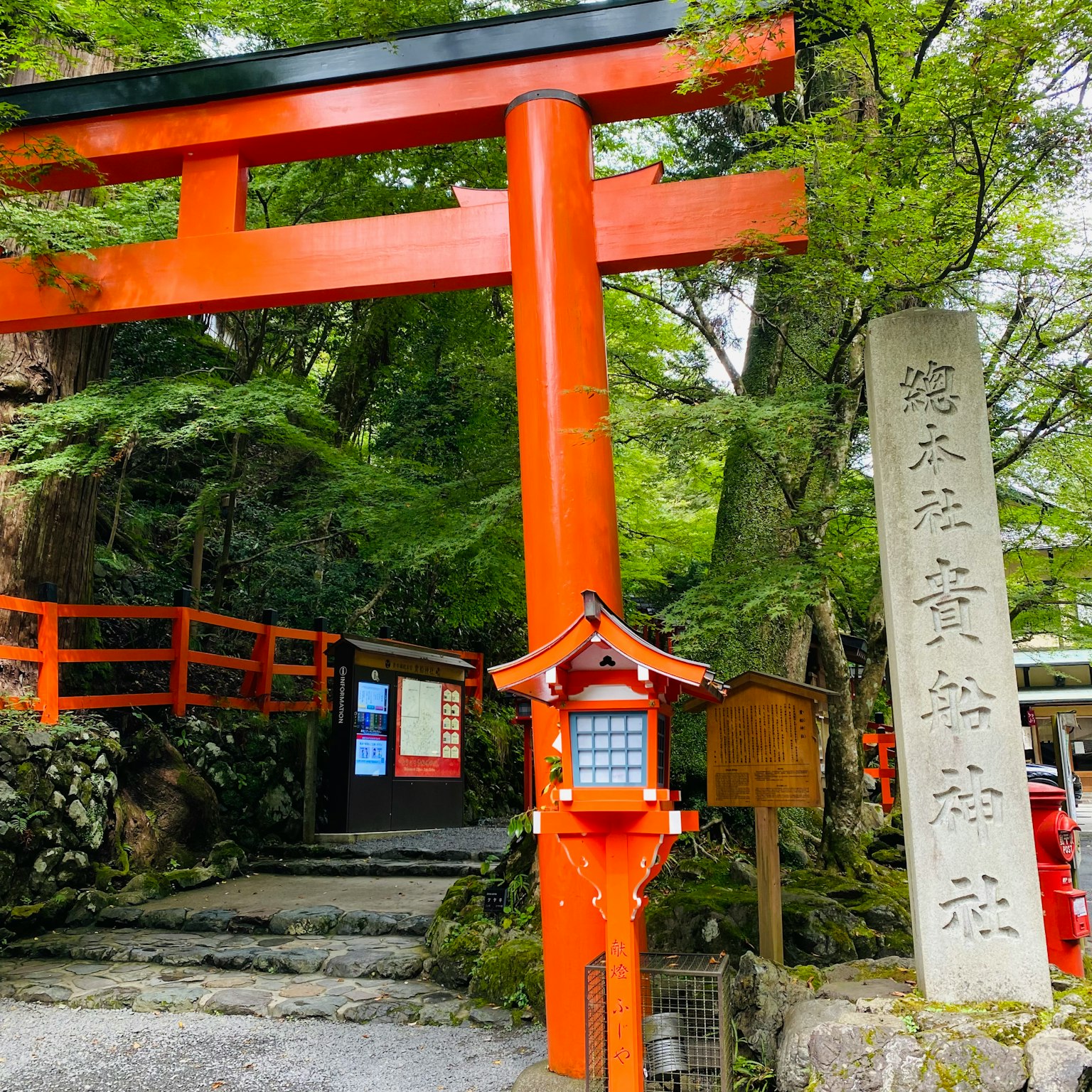 Entrata di un santuario con un torii rosso e un monumento di pietra circondato da una vegetazione lussureggiante