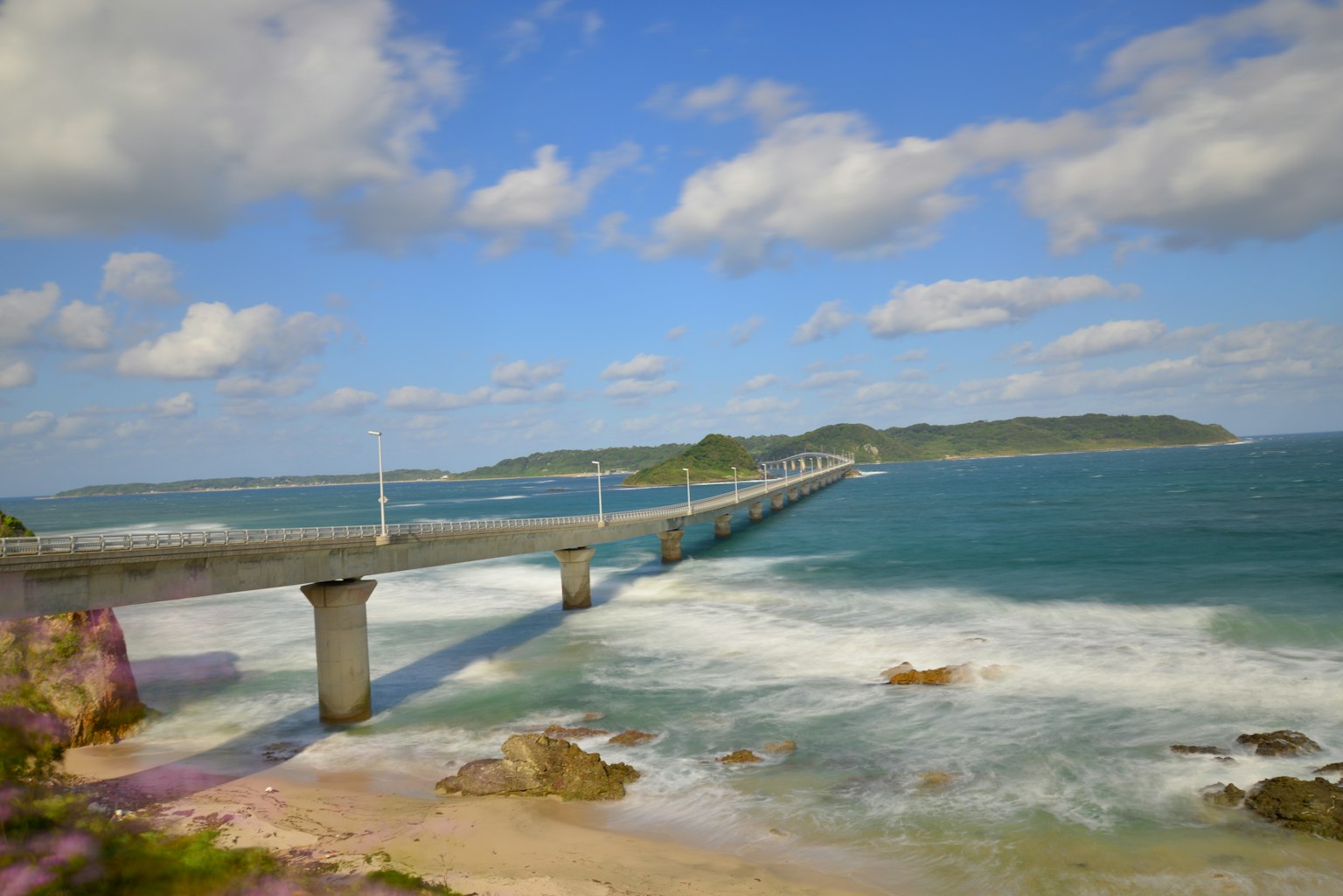 Vista panoramica di un lungo ponte su onde oceaniche blu sotto un cielo parzialmente nuvoloso