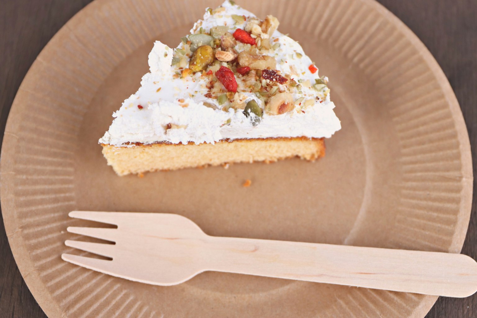 Una fetta di torta guarnita con crema bianca e frutta su un piatto di carta