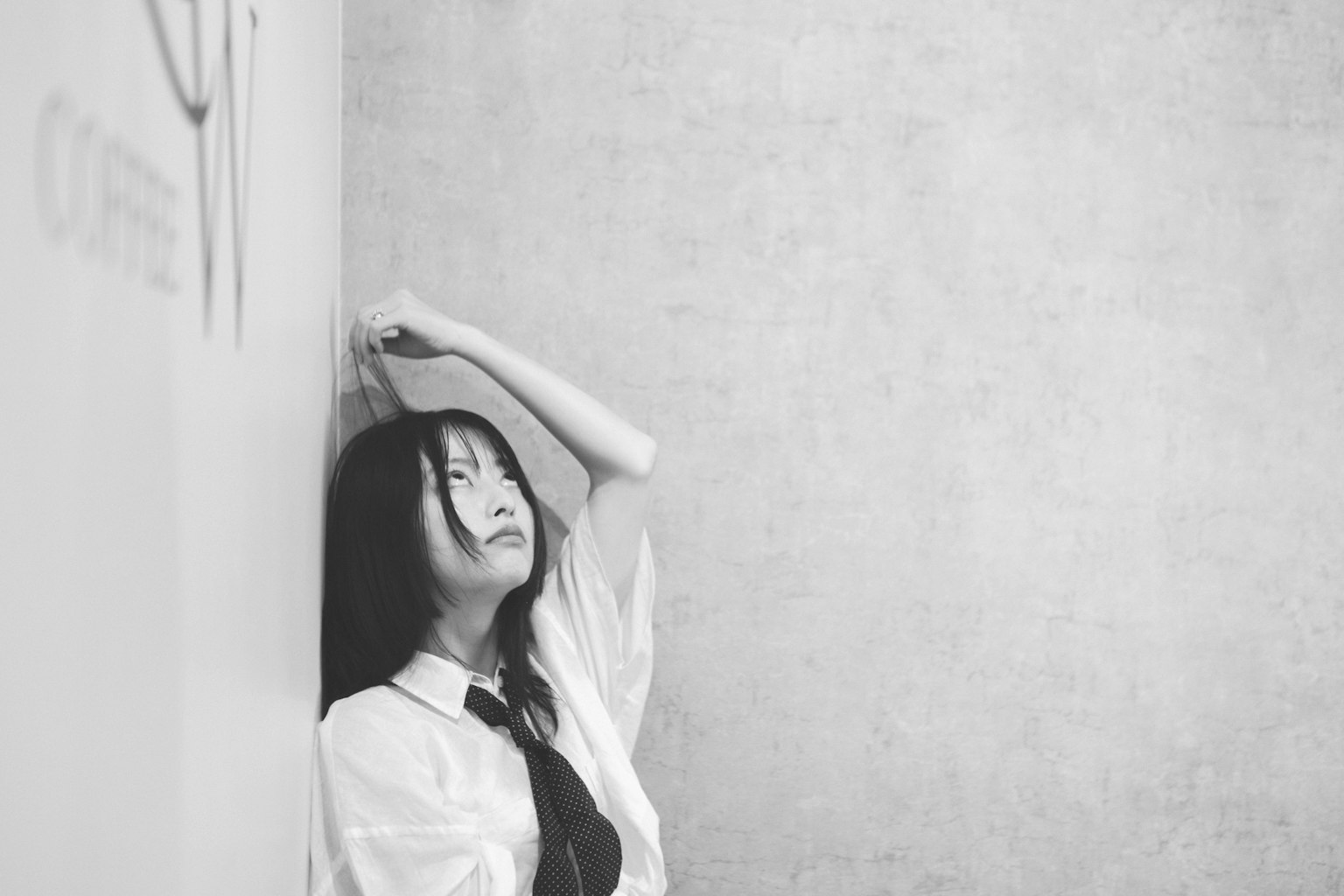 Ảnh đen trắng của một người phụ nữ dựa vào tường với tóc buộc lại