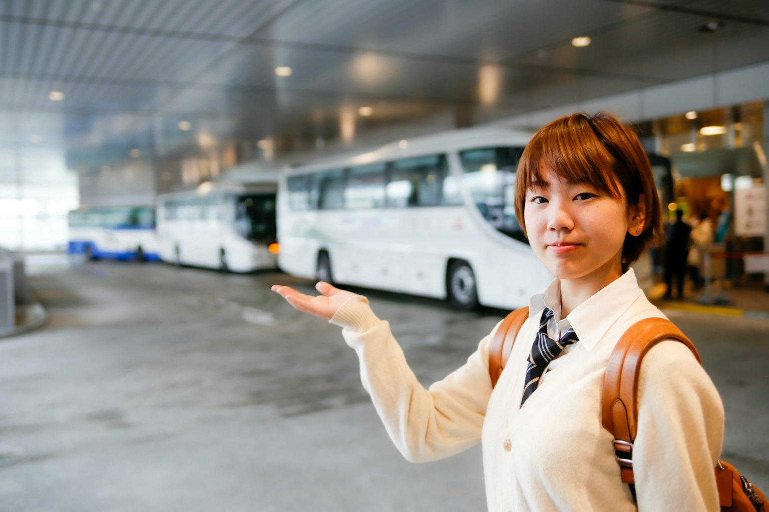 Một người phụ nữ chỉ vào hàng xe buýt màu trắng tại một trạm xe buýt