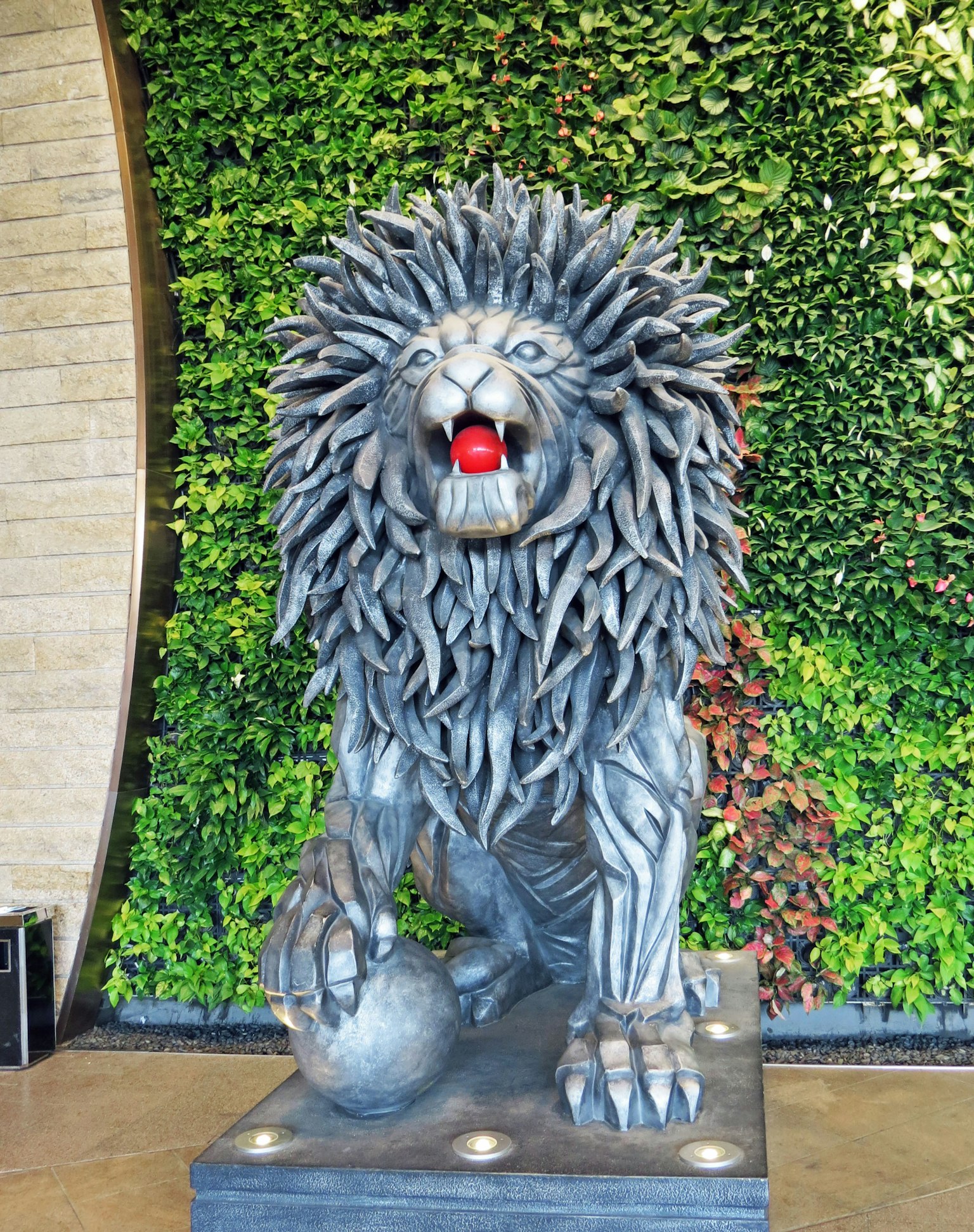 Lion sculpture in front of a green wall holding a red ball in its mouth