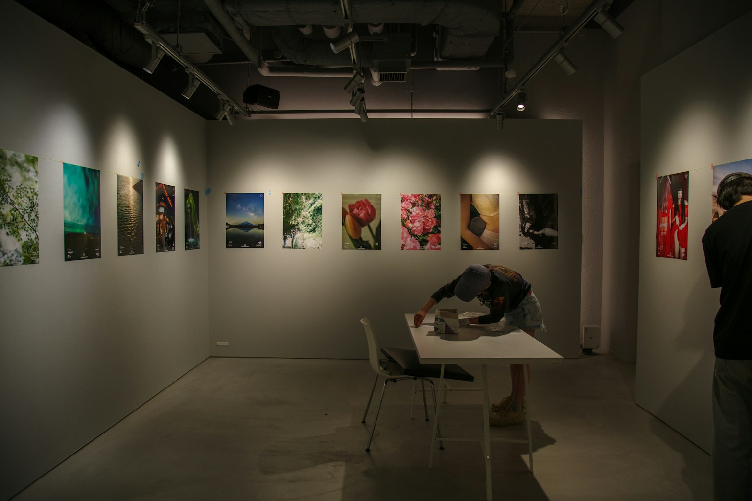 Interior of an art gallery with displayed photographs on the wall and a person working at a table
