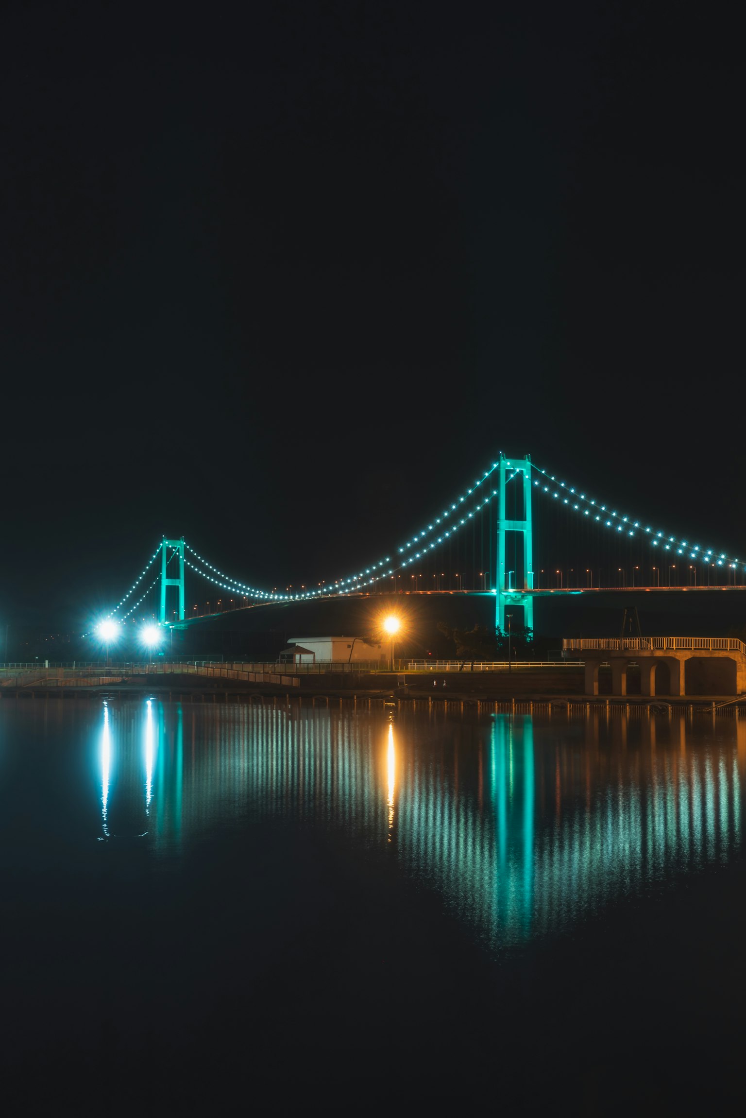 Pemandangan malam jembatan yang diterangi lampu biru yang memantul di atas air