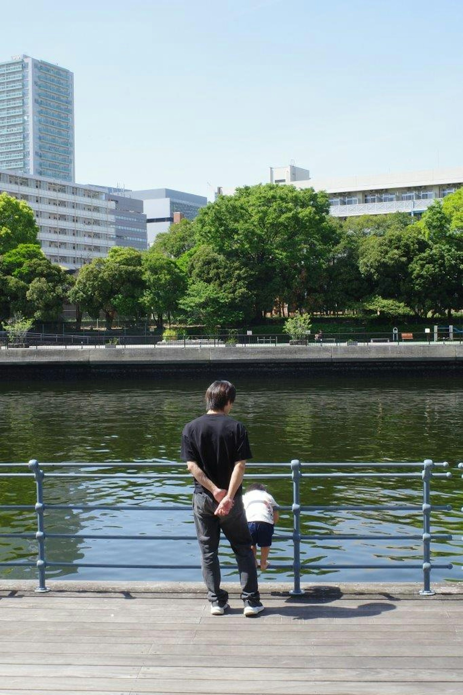 Un uomo e un bambino in piedi vicino a un fiume tranquillo che guardano il paesaggio urbano con vegetazione