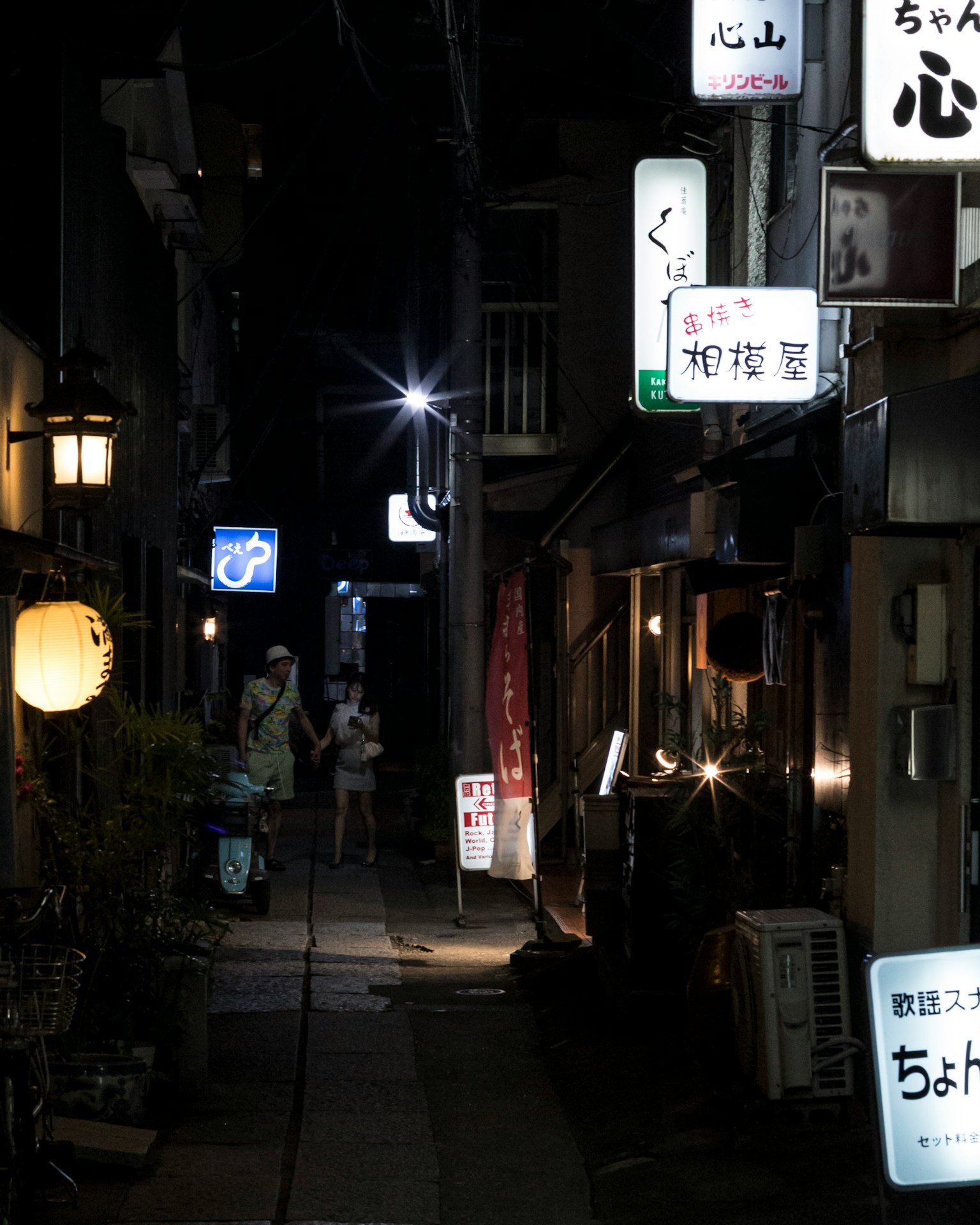 夜の小道に並ぶ飲食店の看板と人々の姿