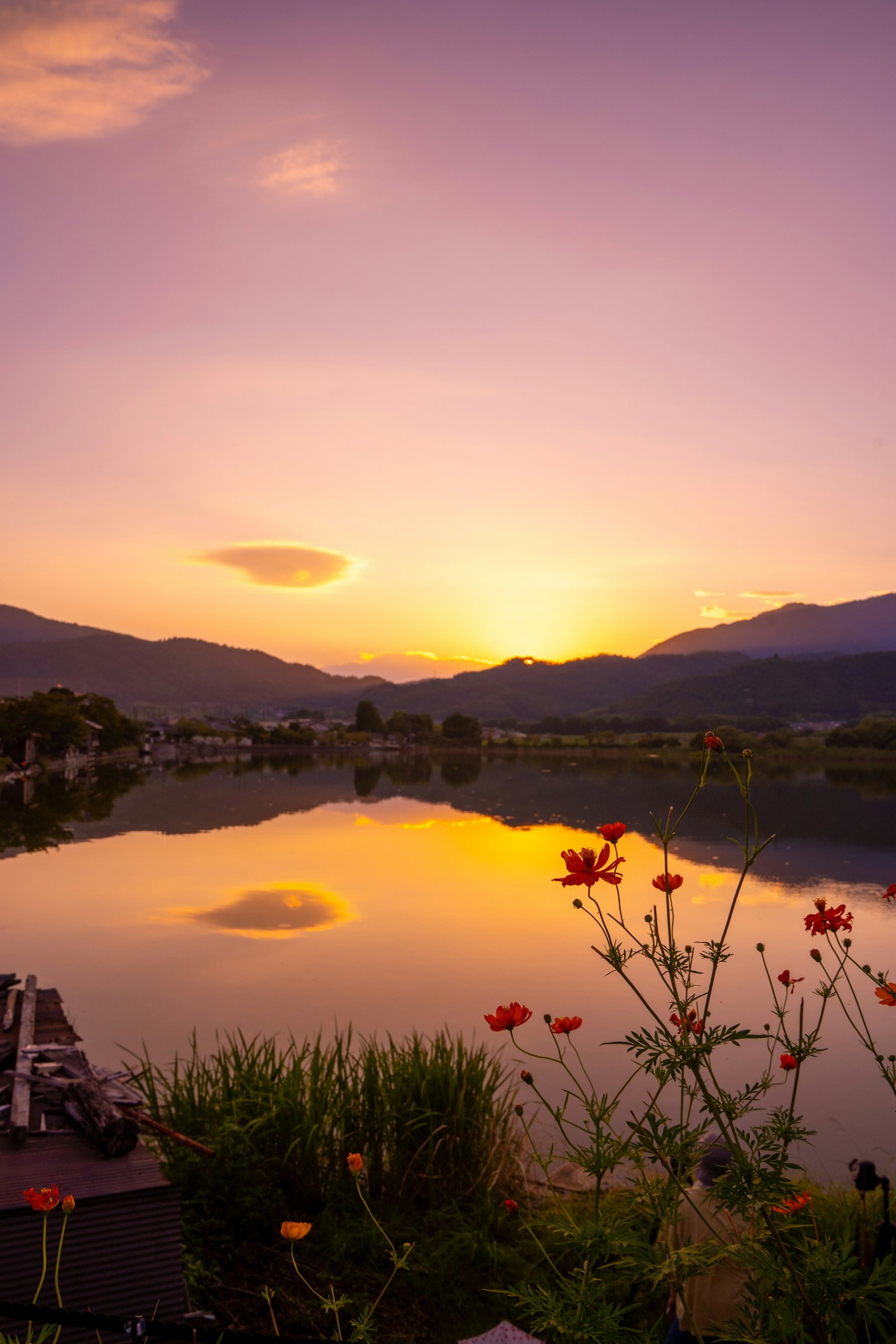 Panorama di un lago al tramonto con fiori e montagne riflesse