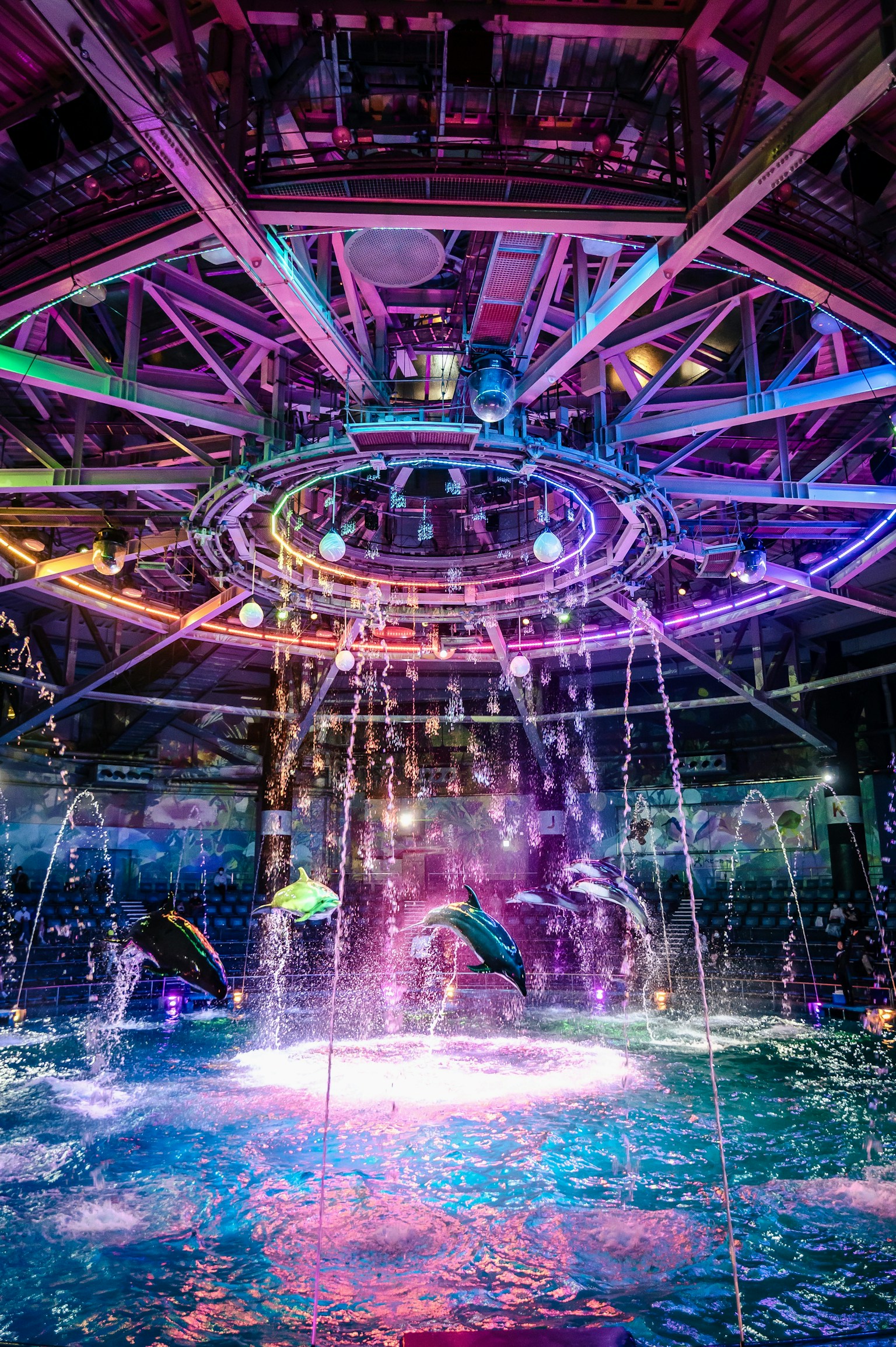 Colorful lighted circular fountain with water jets and decorative structure above