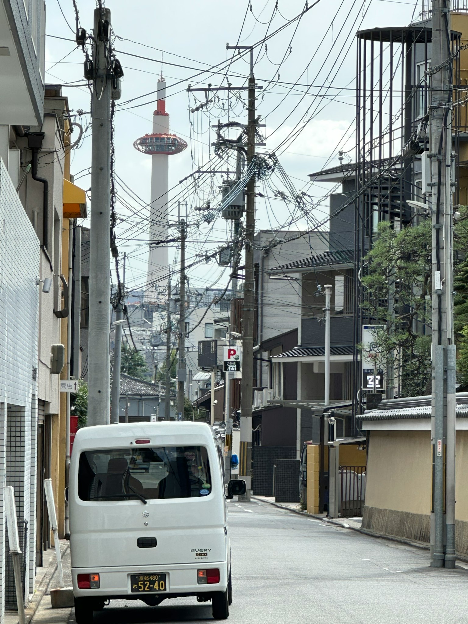 Ein weißer Kleinbus, der in einer engen Straße in Kyoto parkt, mit dem Kyoto Tower im Hintergrund
