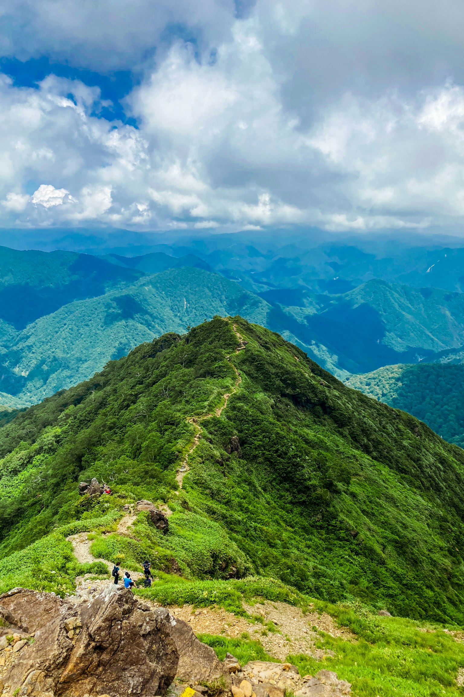 Vista panoramica da un picco montano che mostra una vegetazione lussureggiante e montagne lontane