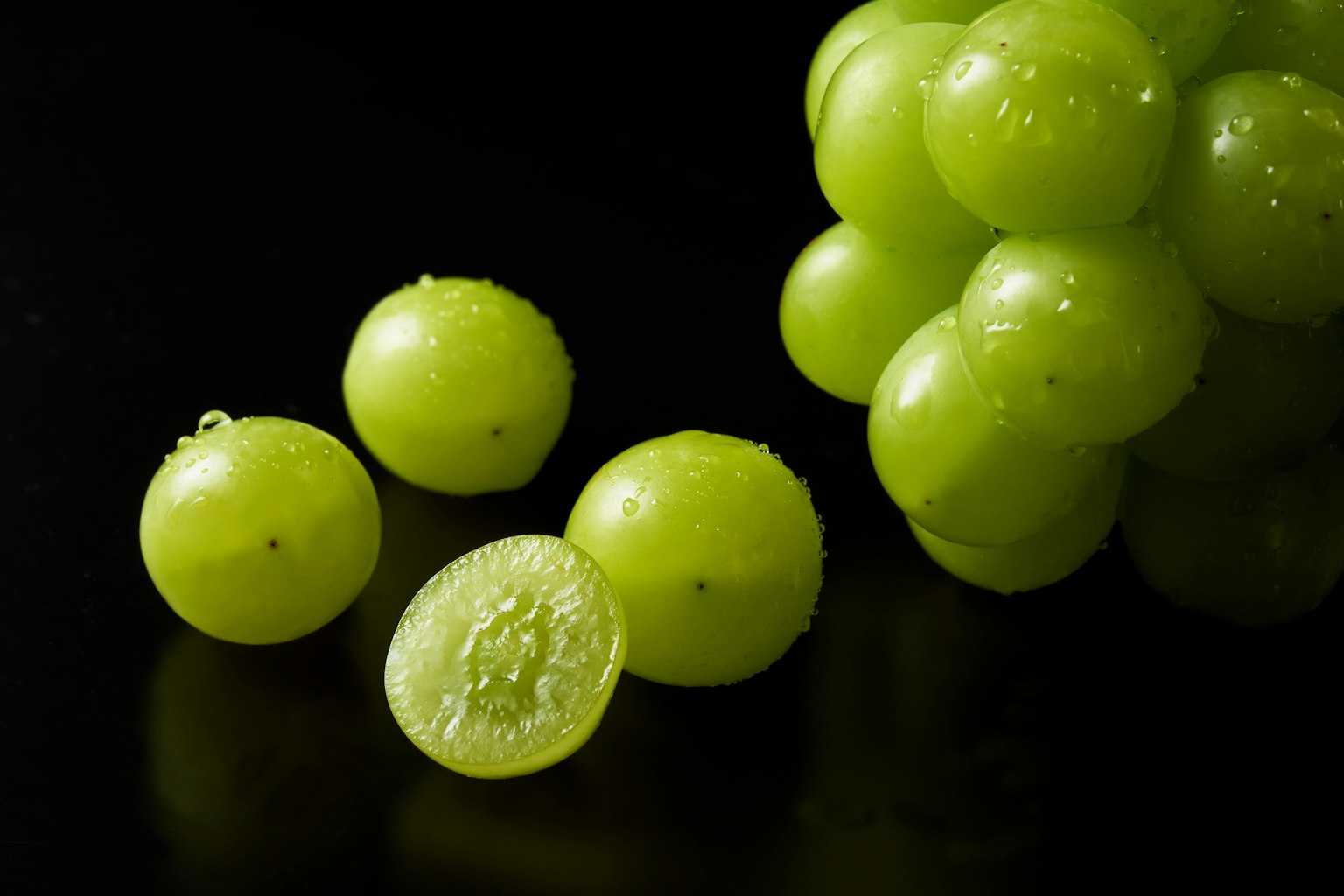 Grappolo di uva verde con gocce d'acqua e un'uva affettata