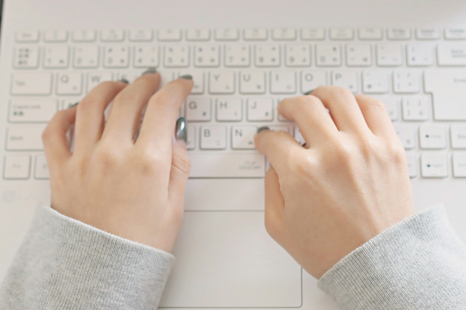 Manos escribiendo en un teclado blanco