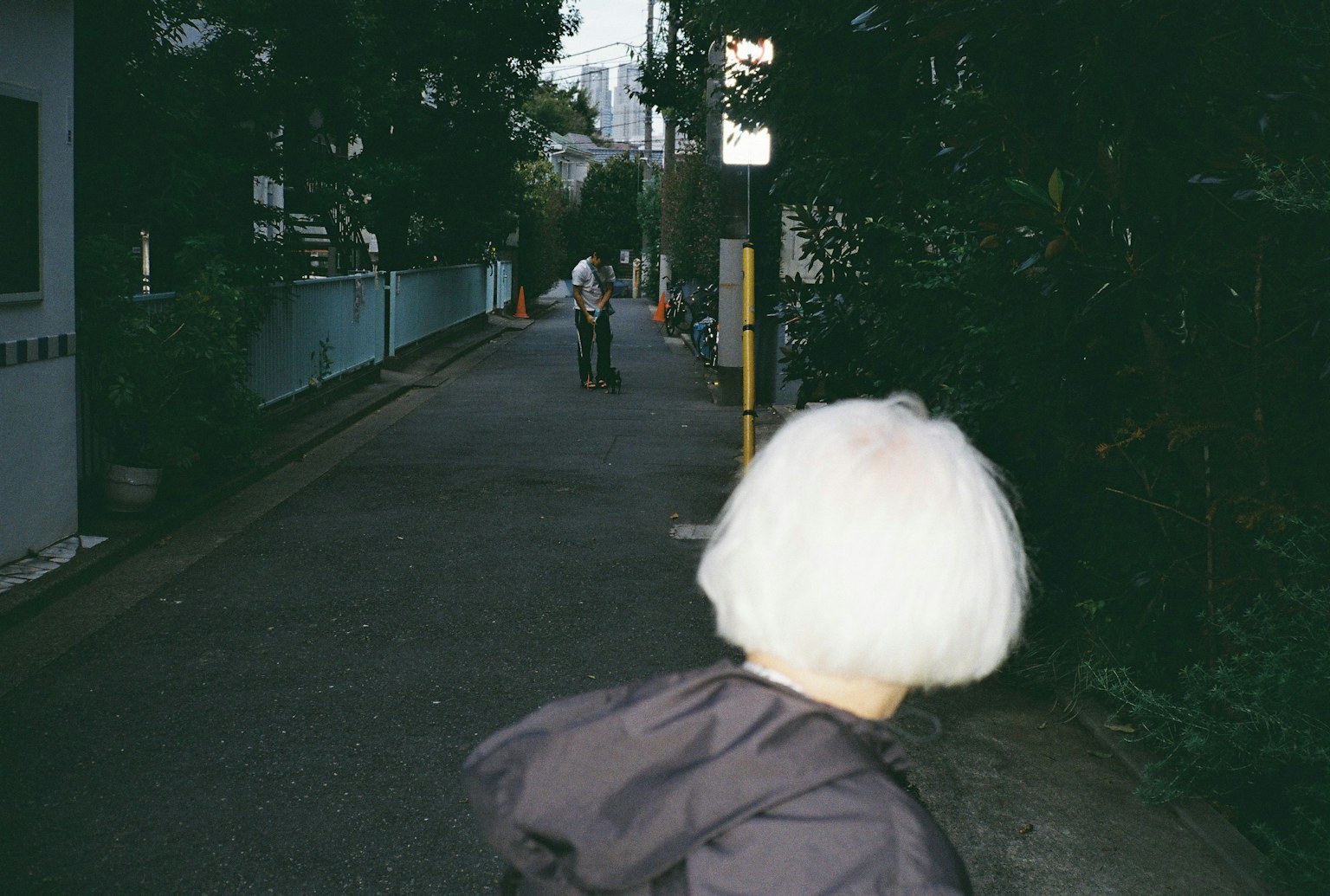 白髪の女性が後ろを振り返る路地の風景