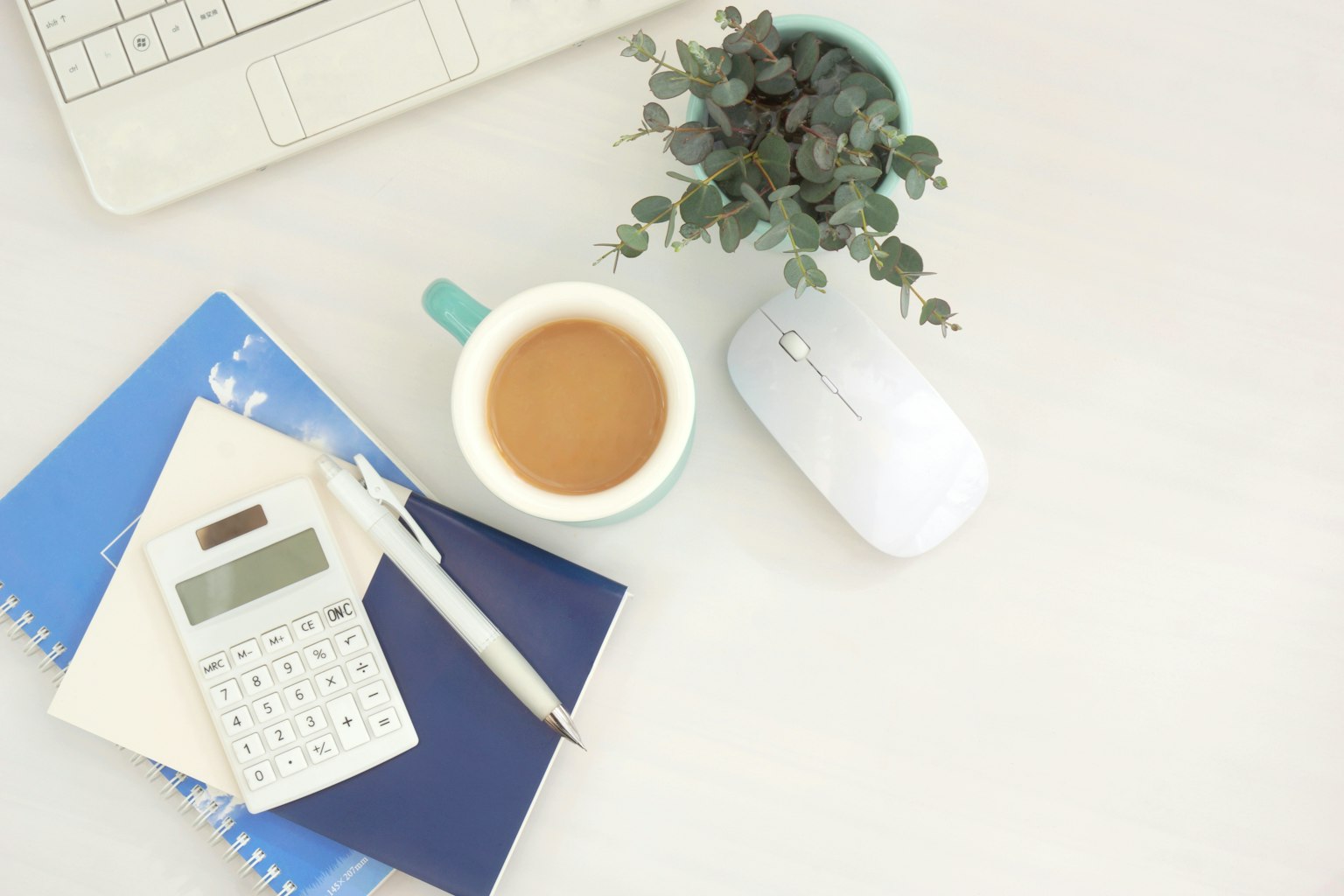 Schreibtisch mit einer Tasse Kaffee einem Taschenrechner Notizbüchern und einer kleinen Pflanze