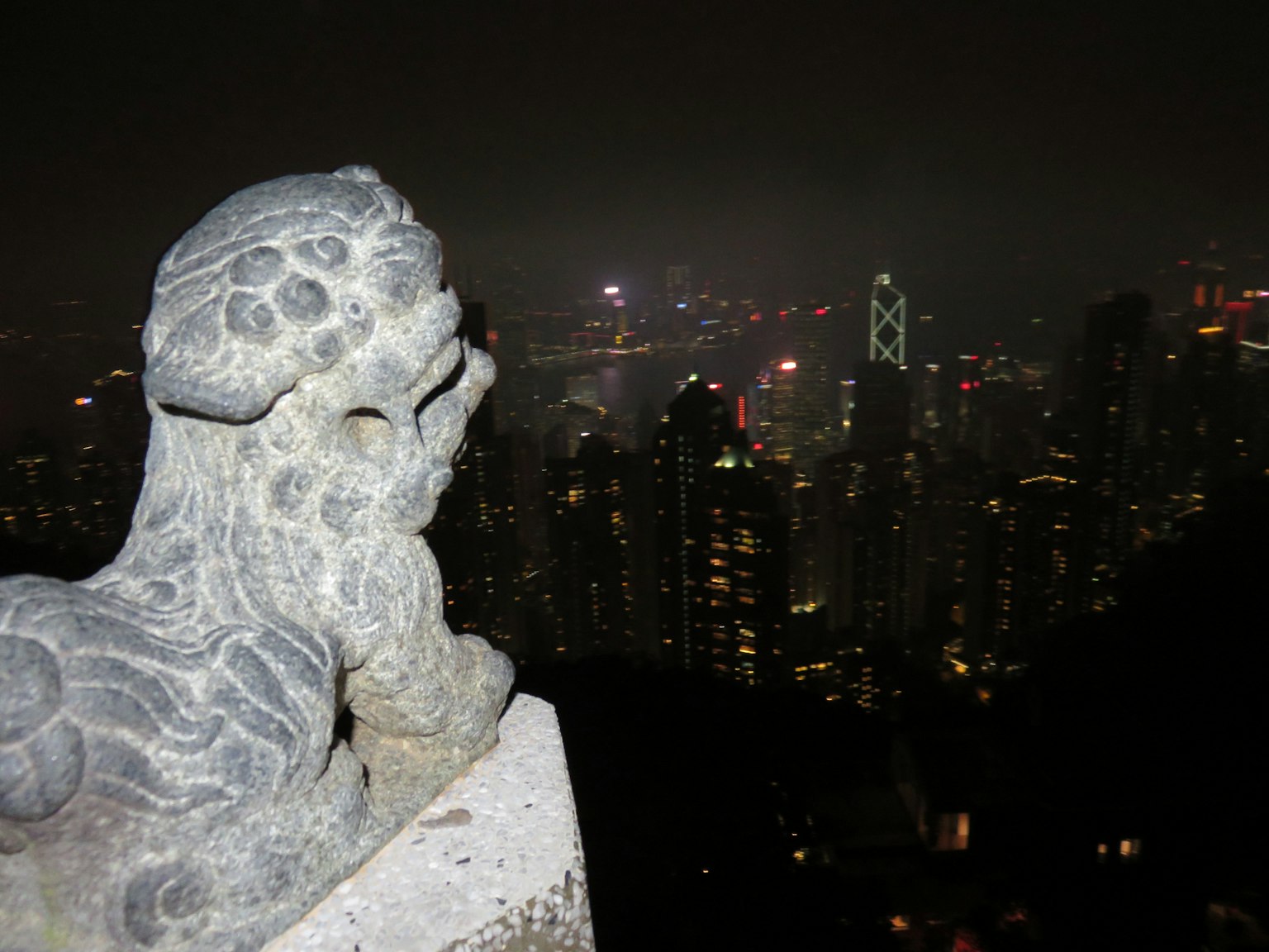 Estatua de león de piedra que observa la vista nocturna del horizonte de Hong Kong
