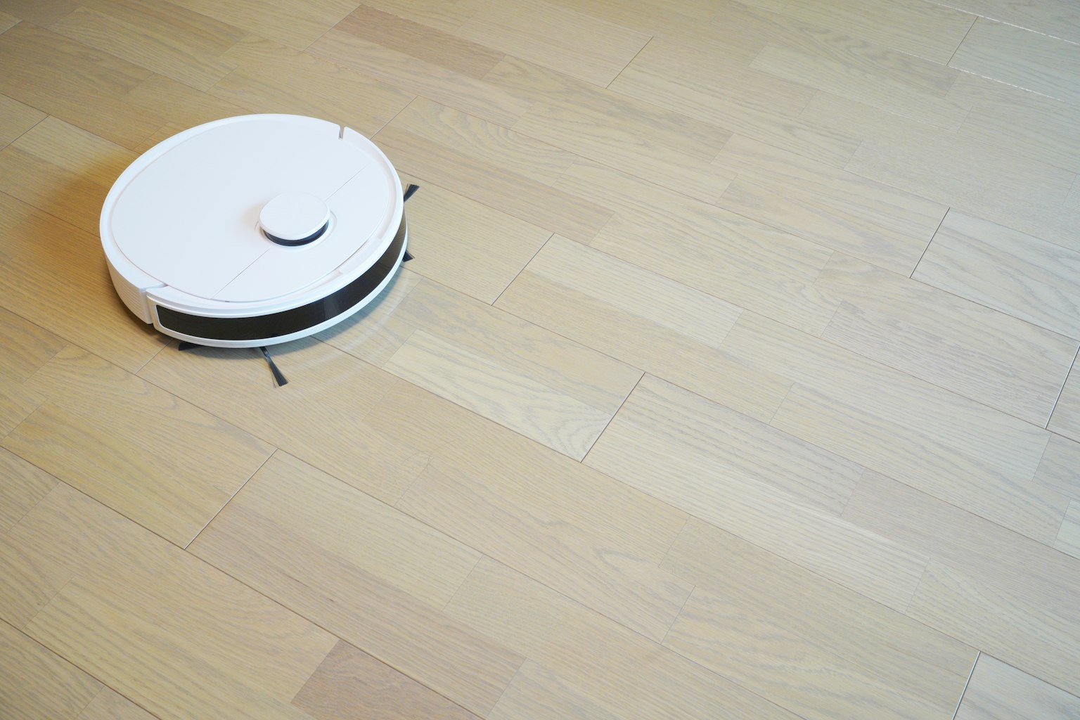 Un aspirateur robot blanc se déplaçant sur un sol en bois