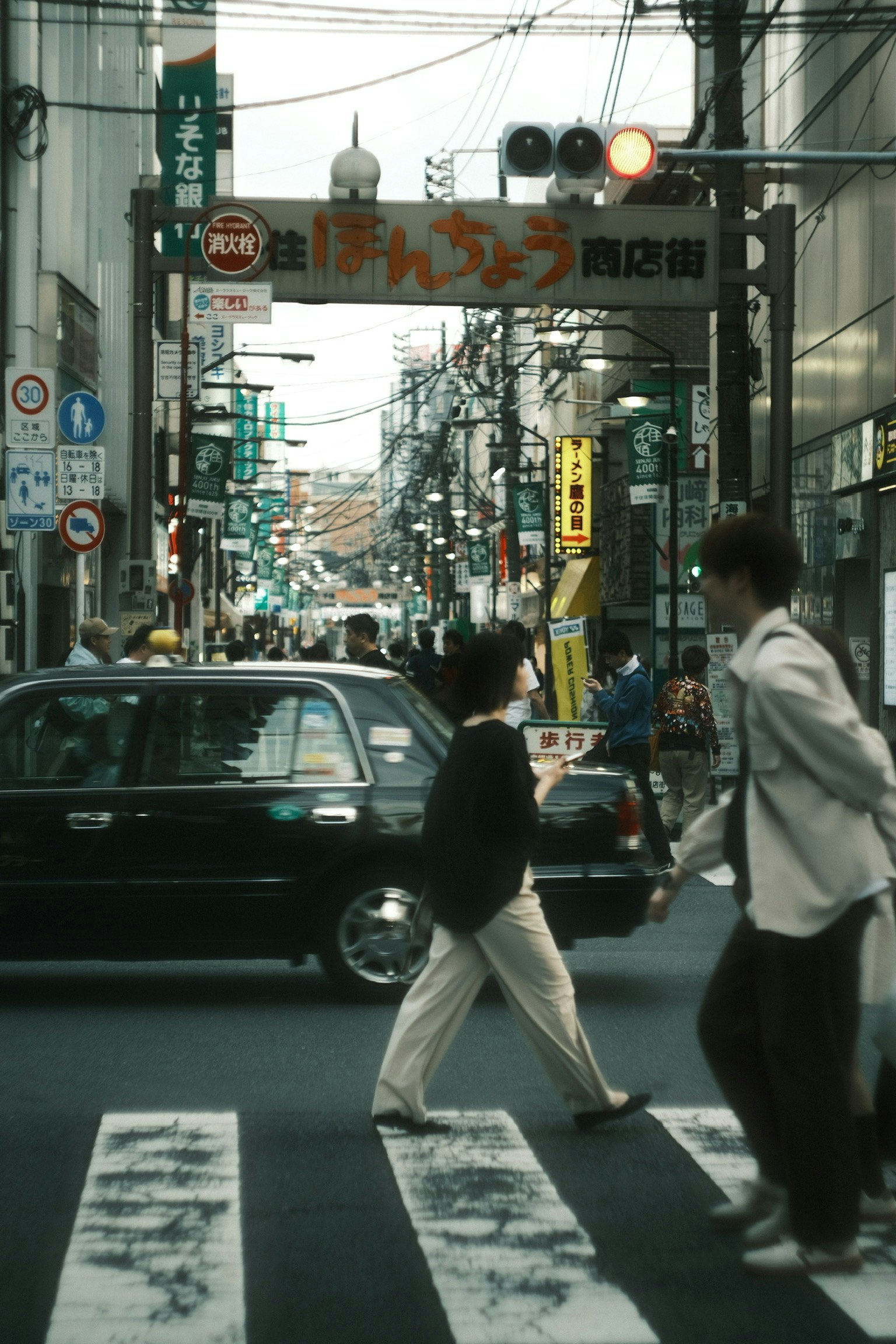 繁華街の交差点で歩行者が横断歩道を渡る様子 車と看板が見える