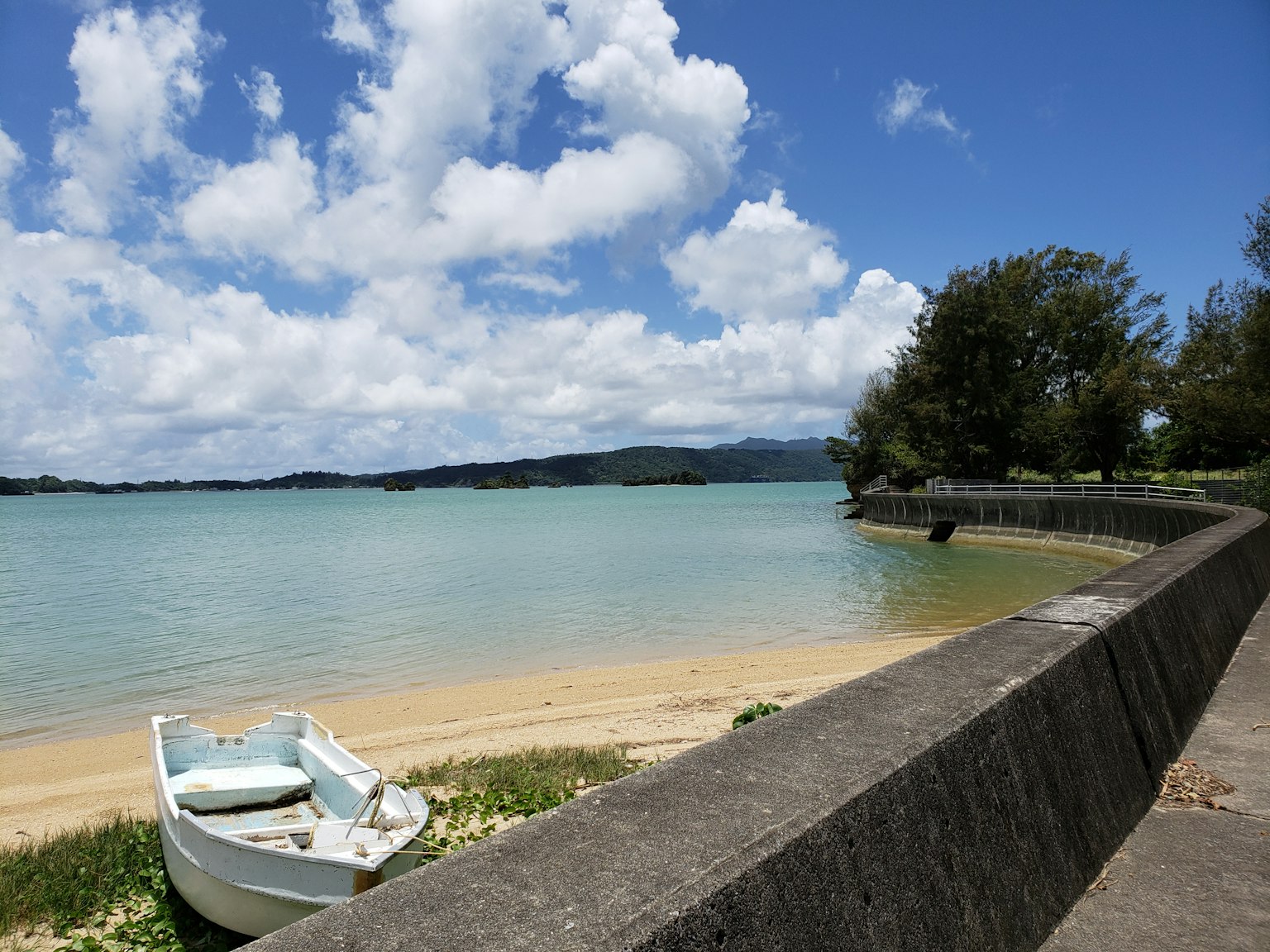 Malersiche Strandansicht mit blauem Meer und weißen Wolken Kleines Boot am Ufer und Steinpier