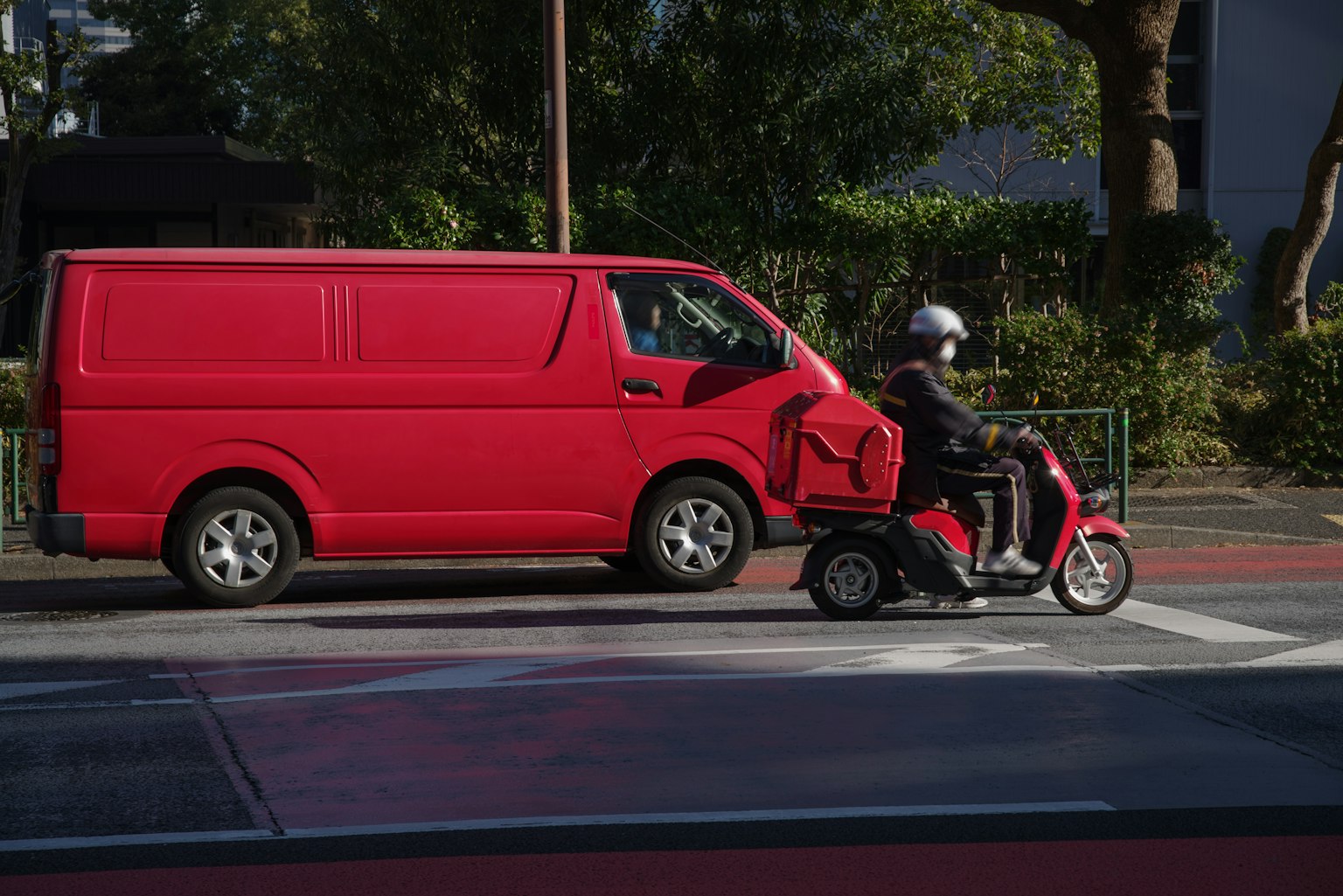 Un furgone rosso e uno scooter rosso che viaggiano affiancati in un contesto urbano