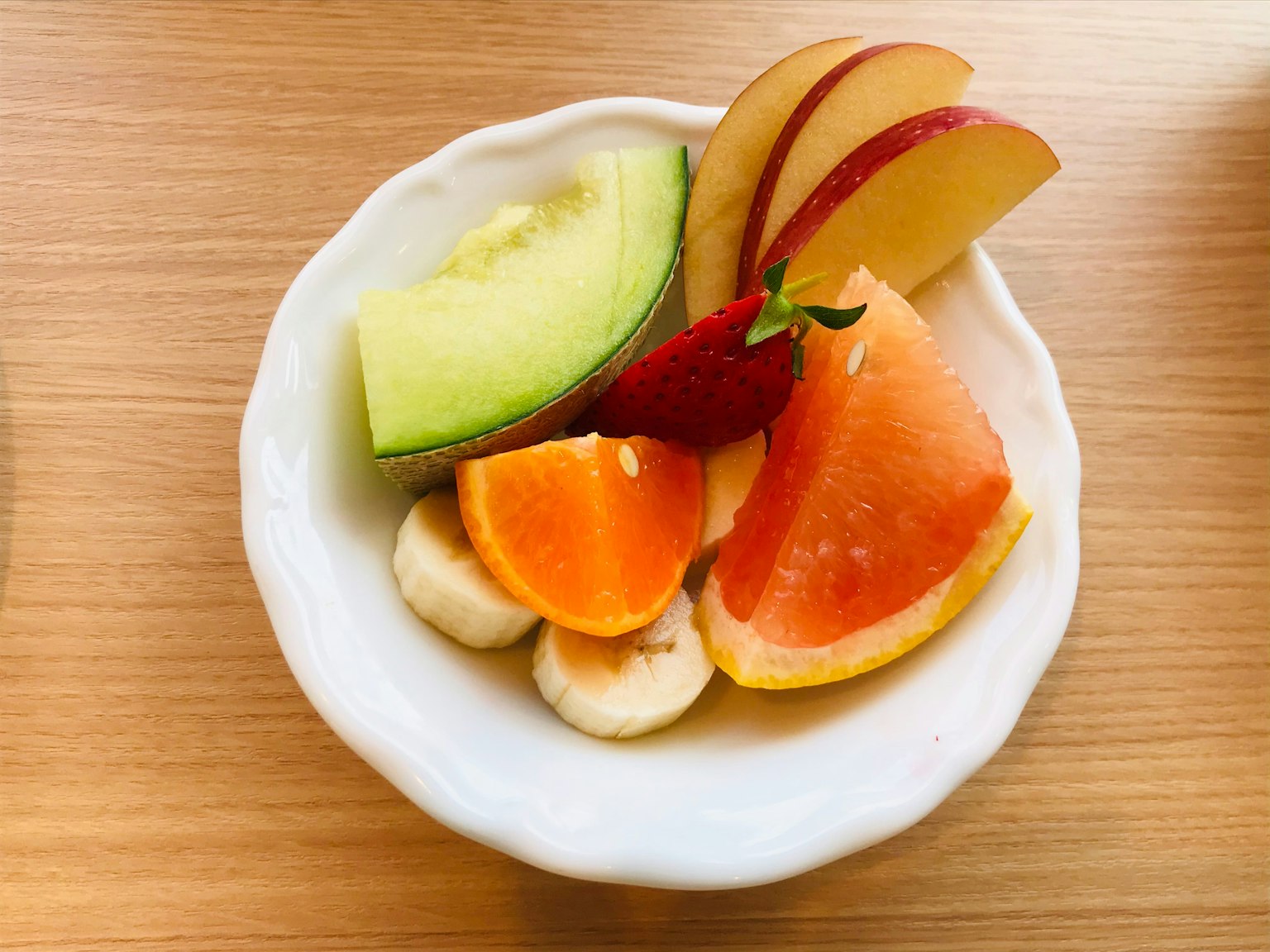 Salad buah berwarna-warni dalam mangkuk putih dengan melon, apel, pisang, jeruk, dan grapefruit