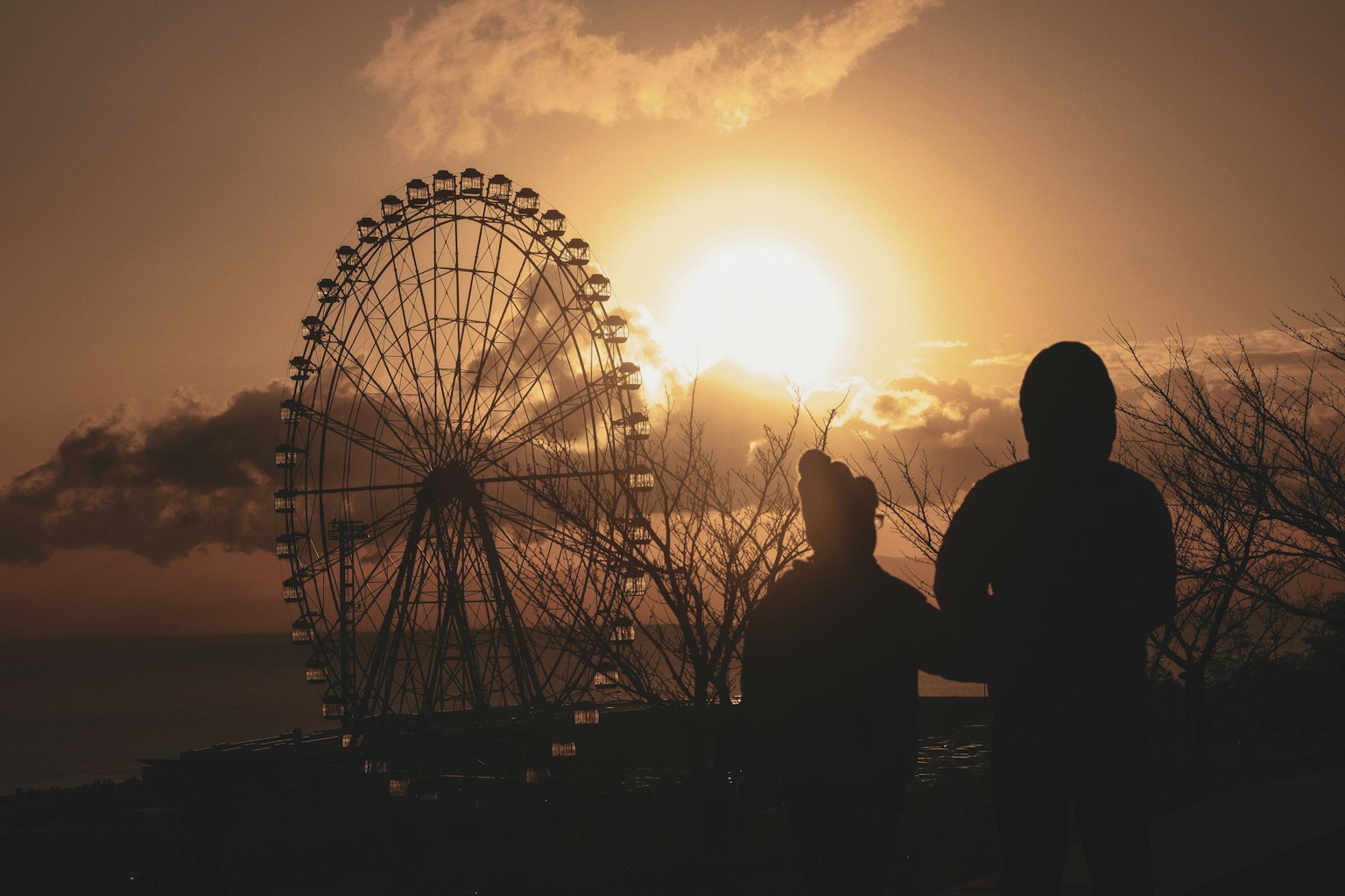 Silhouette d'un couple avec une grande roue contre un coucher de soleil