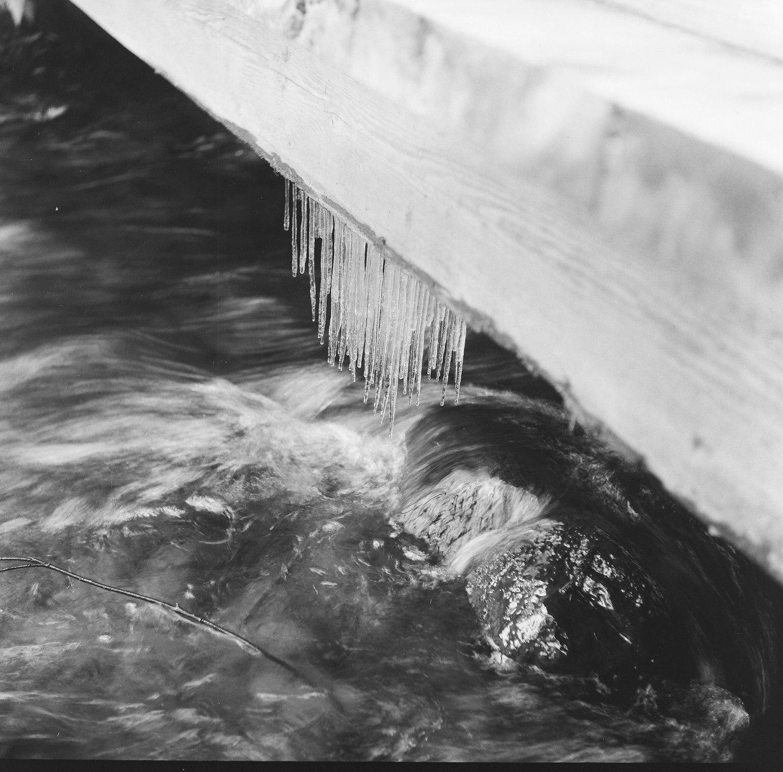 Eiszapfen hängen von einer Holzstruktur über fließendem Wasser