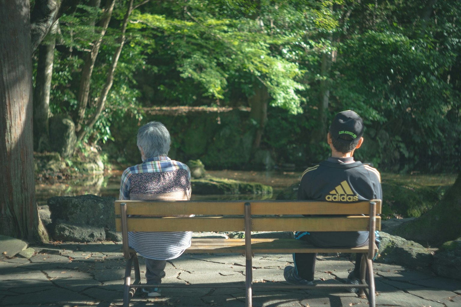 兩個人坐在公園長椅上,四周被郁郁蔥蔥的綠色包圍