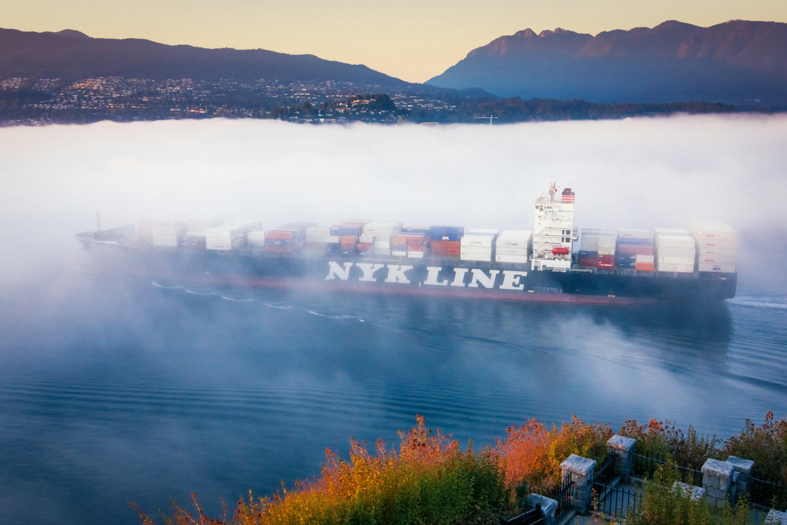 Buque portacontenedores NTK Line navegando a través de la niebla con montañas al fondo