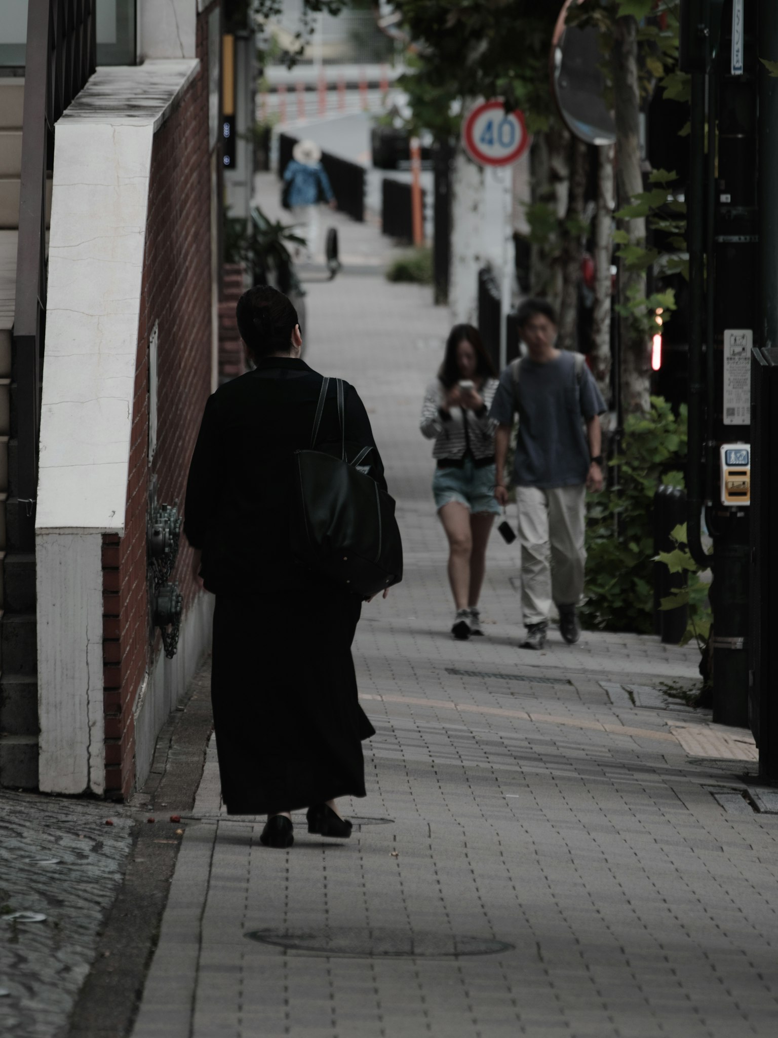 Una persona in abiti neri che cammina per strada con una giovane coppia nelle vicinanze
