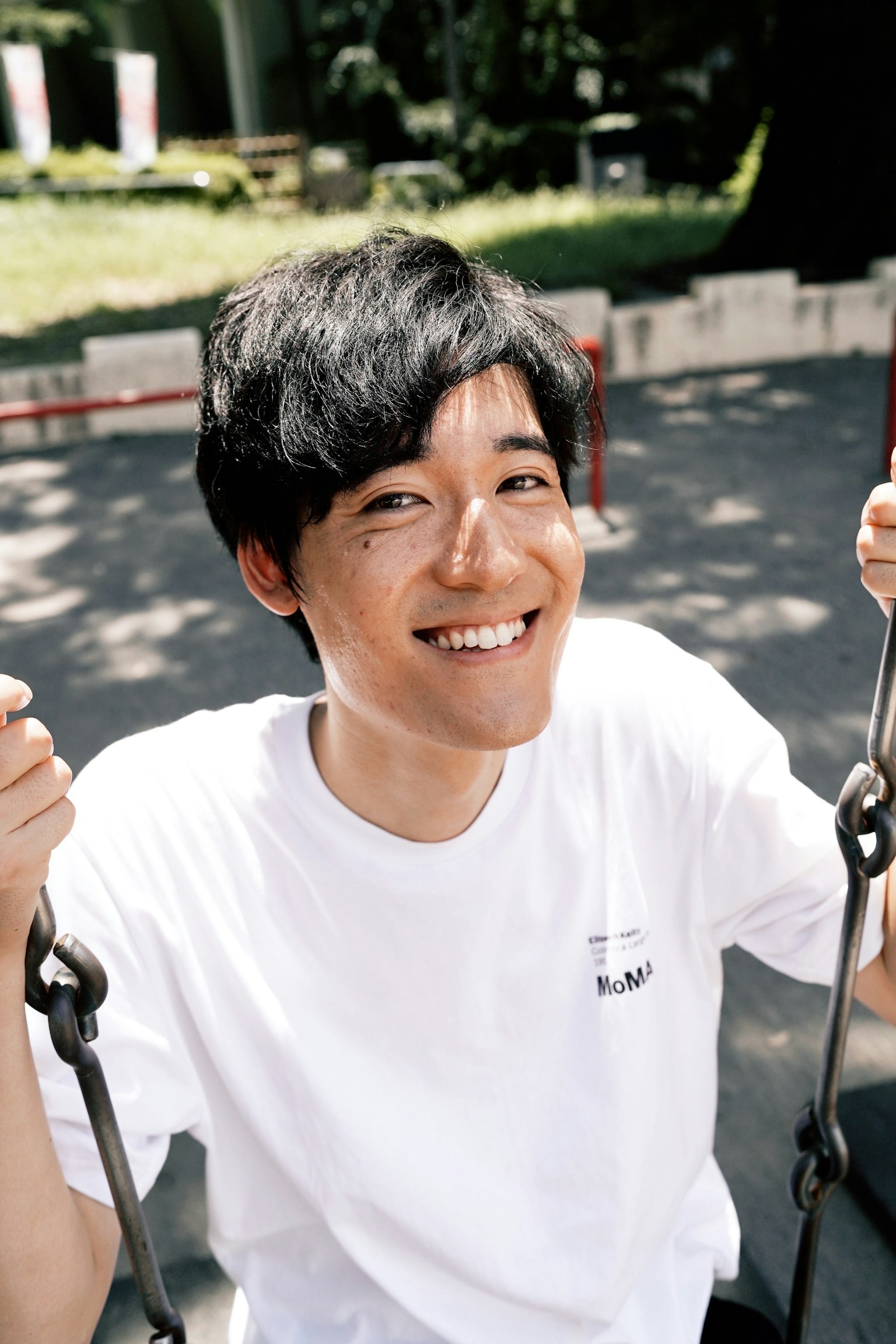 公園のブランコに座っている若い男性が笑顔でカメラを見つめている