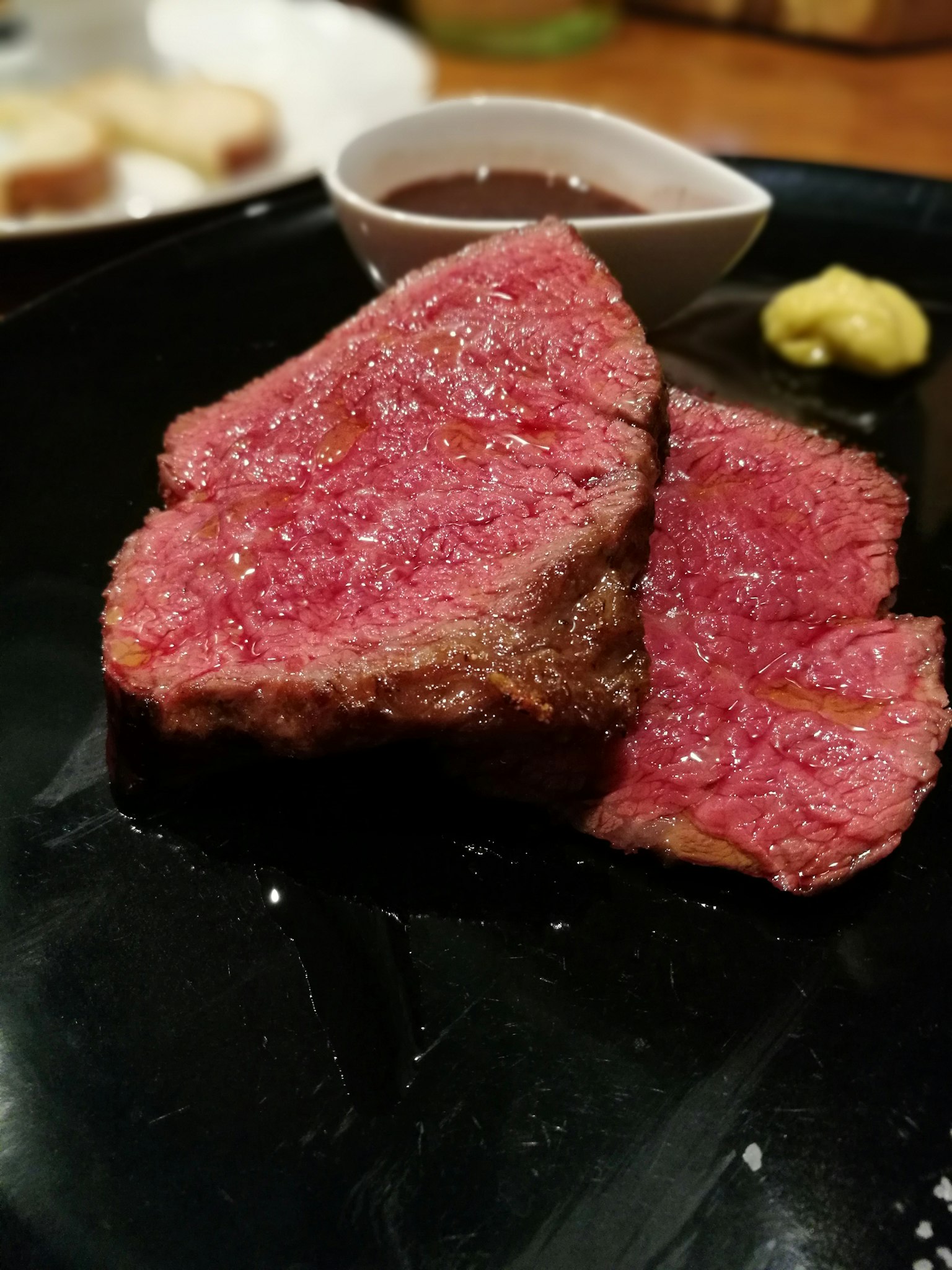 Viande tranchée sur une assiette noire avec sauce et moutarde
