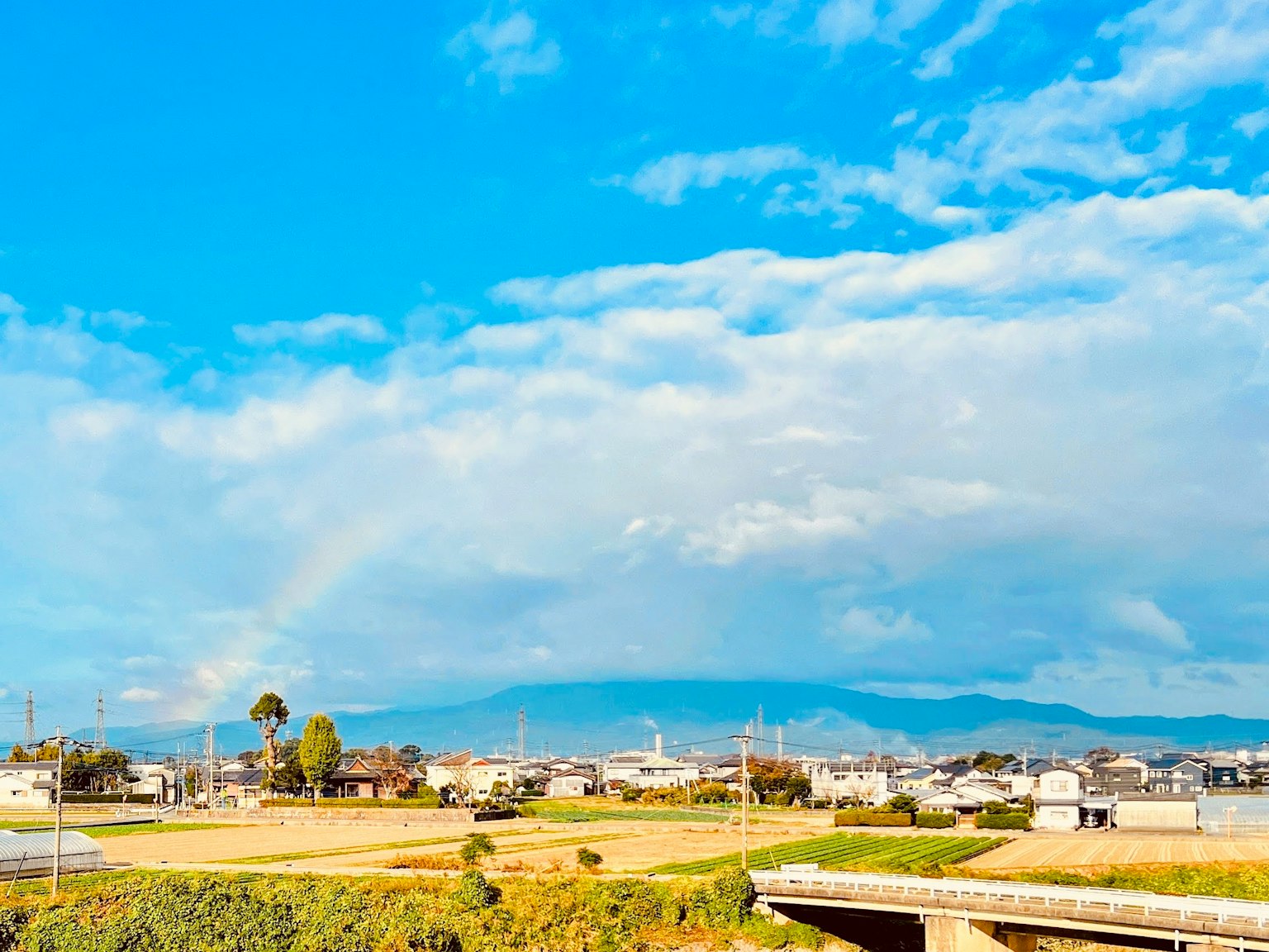 藍天與雲彩下，農村田野上方的彩虹風景