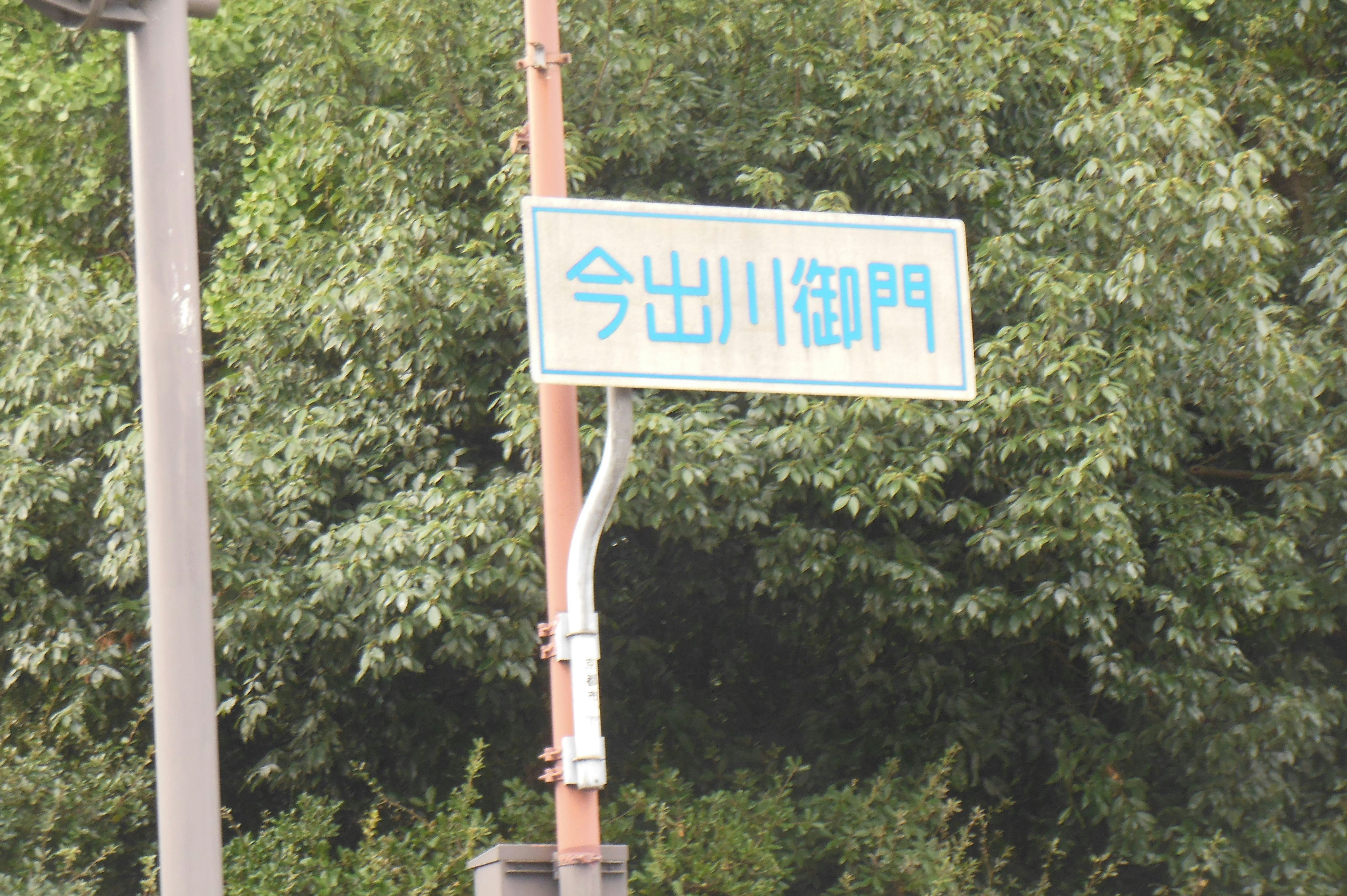 sign reading “Imadegawa Gomon” in front of green hedges