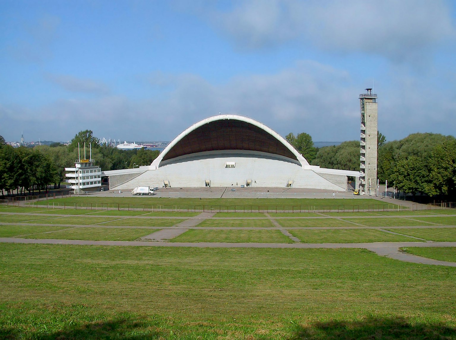 Modern open-air concert hall with curved roof and tower set in a grassy landscape