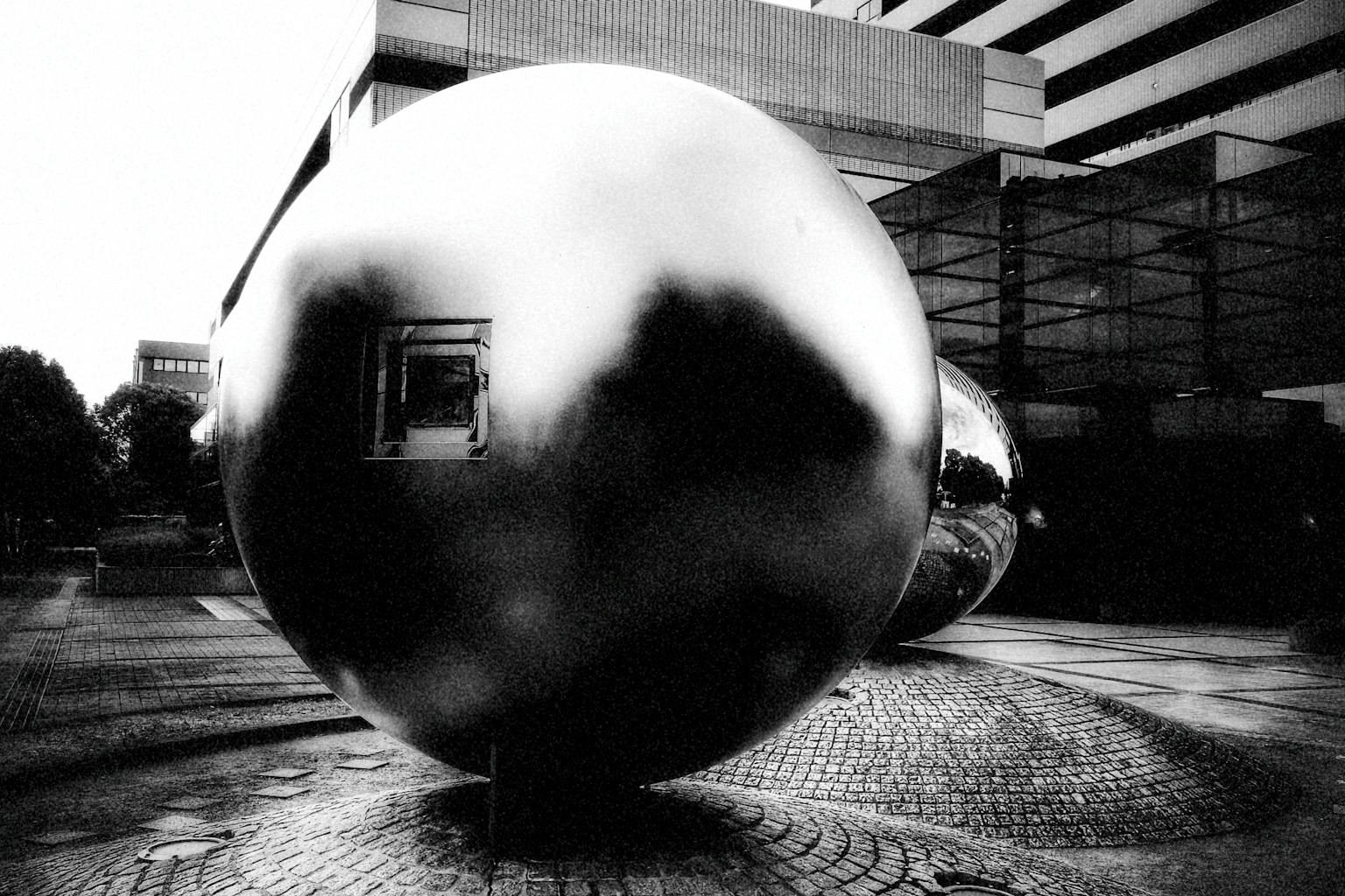 Large metallic sphere in black and white standing amid urban landscape