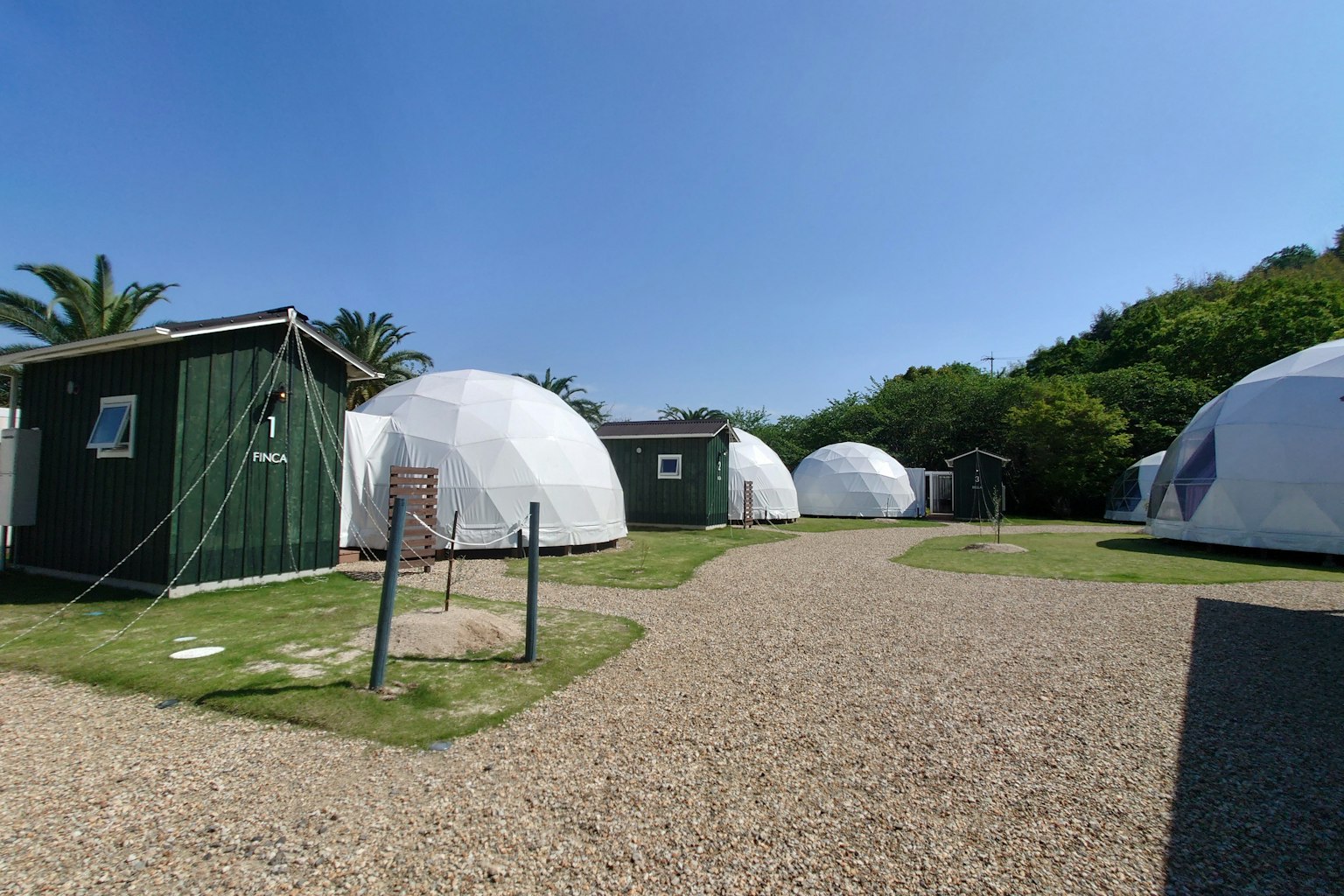 Scenic view of white dome-shaped accommodations surrounded by green huts and clear blue sky