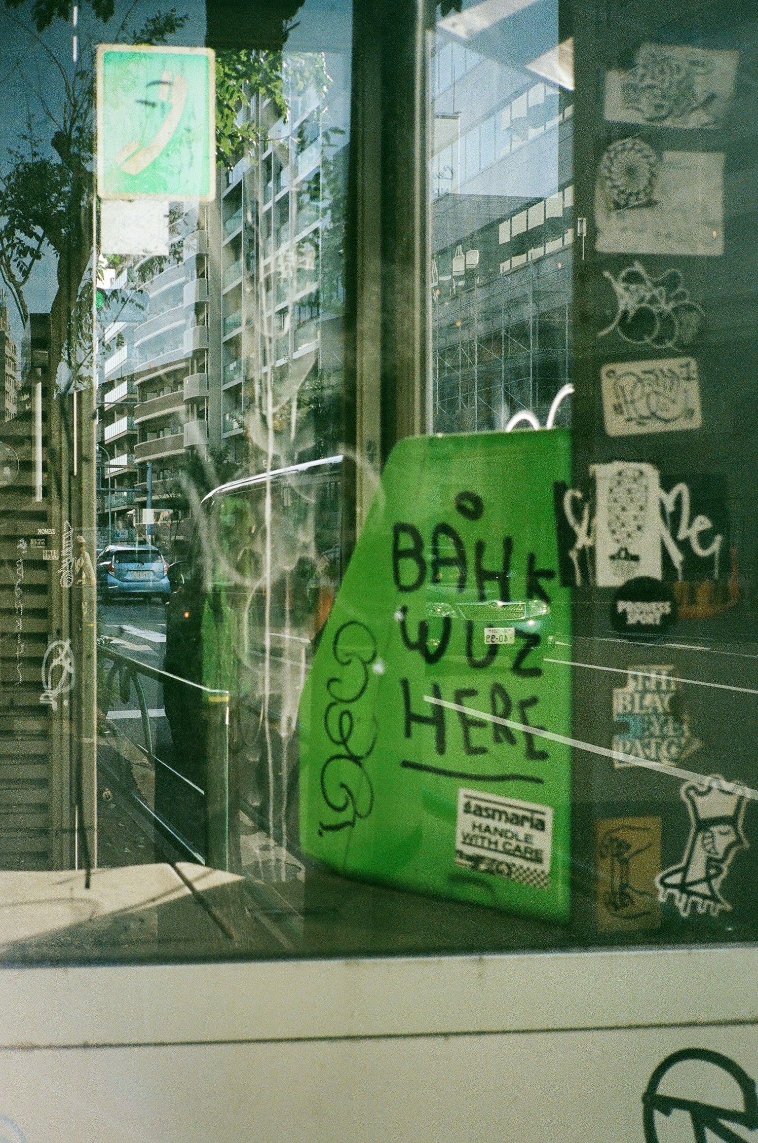 Pannello verde con il testo "BAHK WUZ HERE" visibile attraverso una finestra di un negozio stile arte di strada