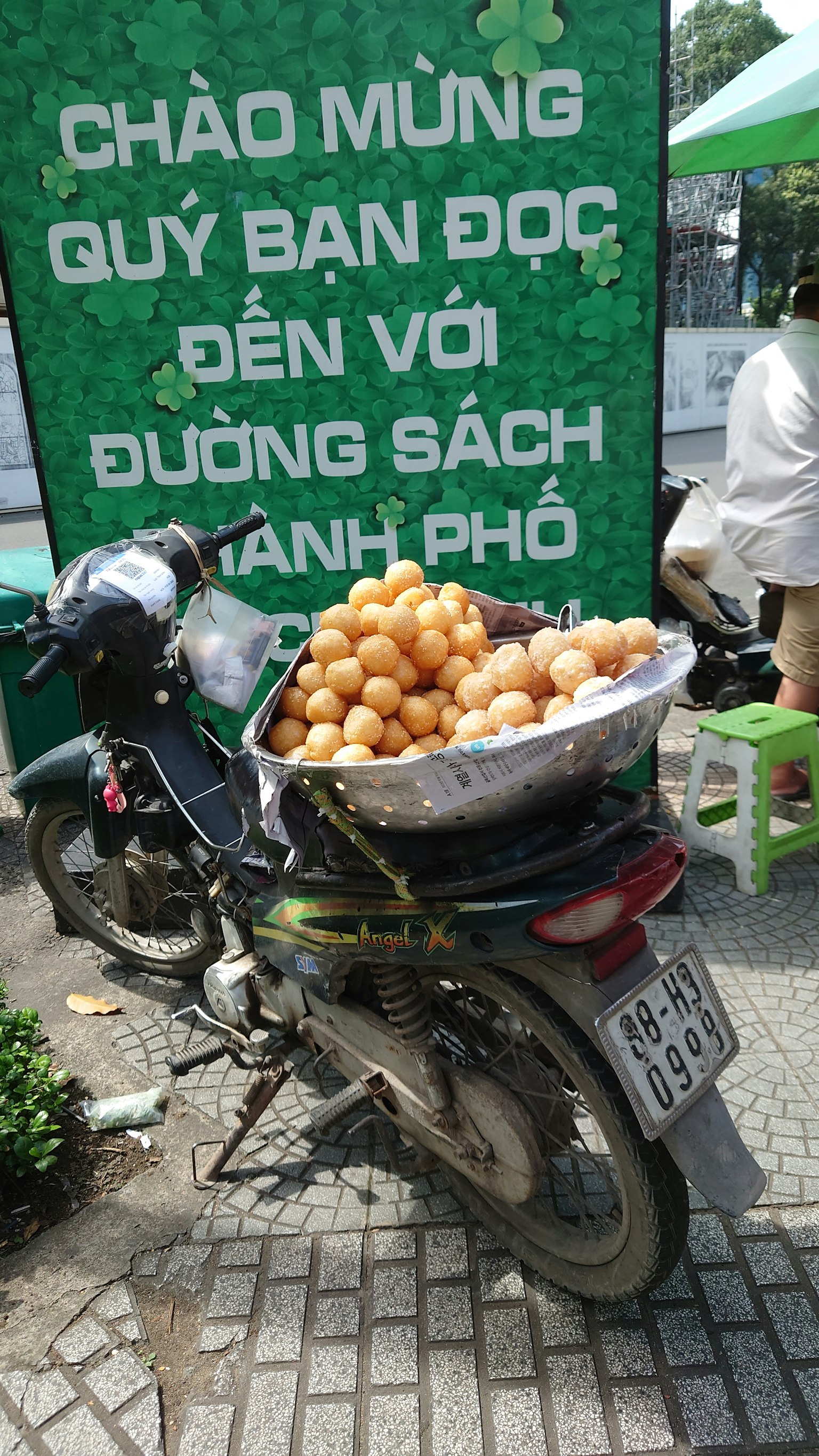 Ein Motorrad mit einer Obstladung in einem Korb vor einem grünen Schild mit vietnamesischem Text