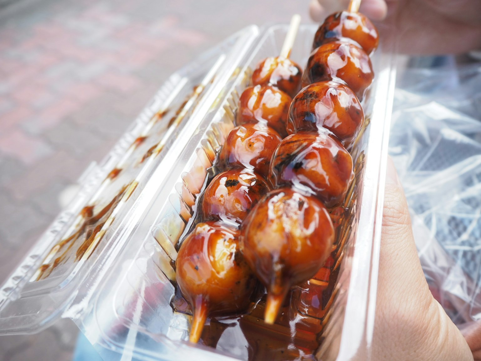 Dango infilzato ricoperto di salsa dolce tenuto in mano
