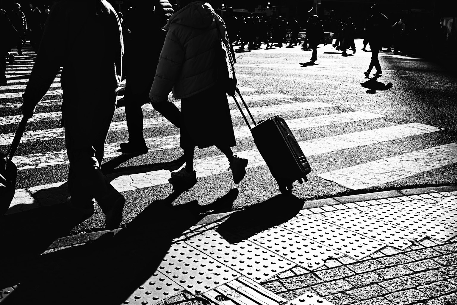 Siluetas de personas caminando en un paso de peatones con una maleta