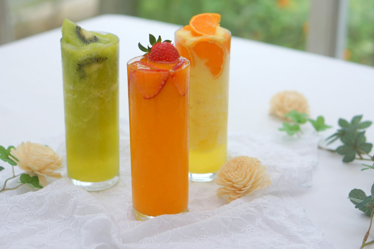Trois cocktails colorés dans des verres hauts sur une table avec des garnitures