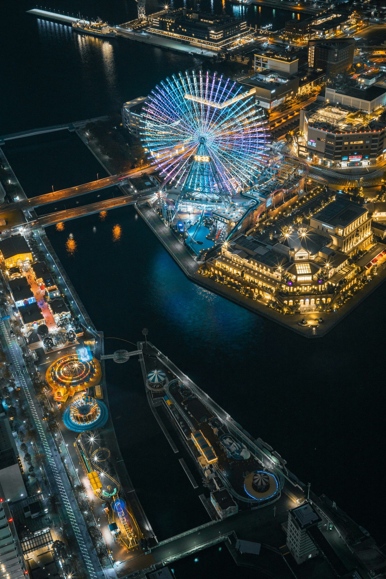 Vue aérienne d'une grande roue colorée et d'un parc d'attractions au bord de l'eau la nuit