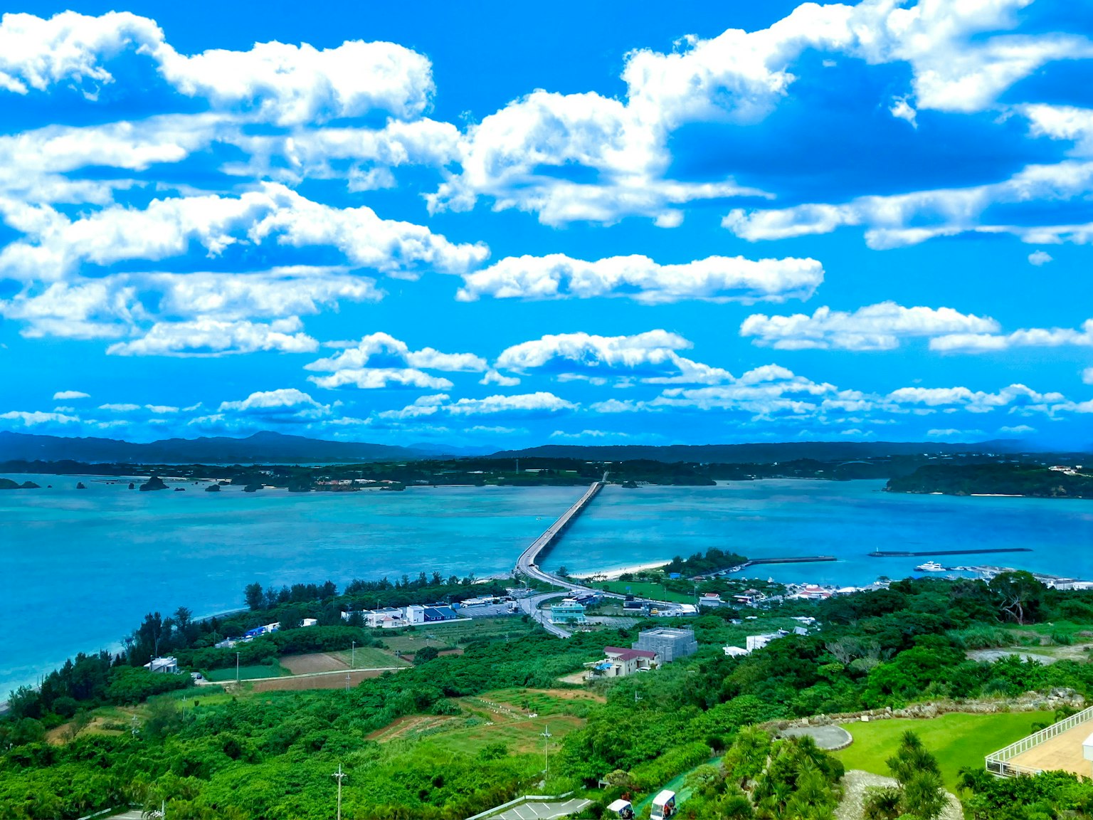 Malerei von blauem Meer und Himmel mit weißen Wolken üppigem grünem Land und einer Brücke