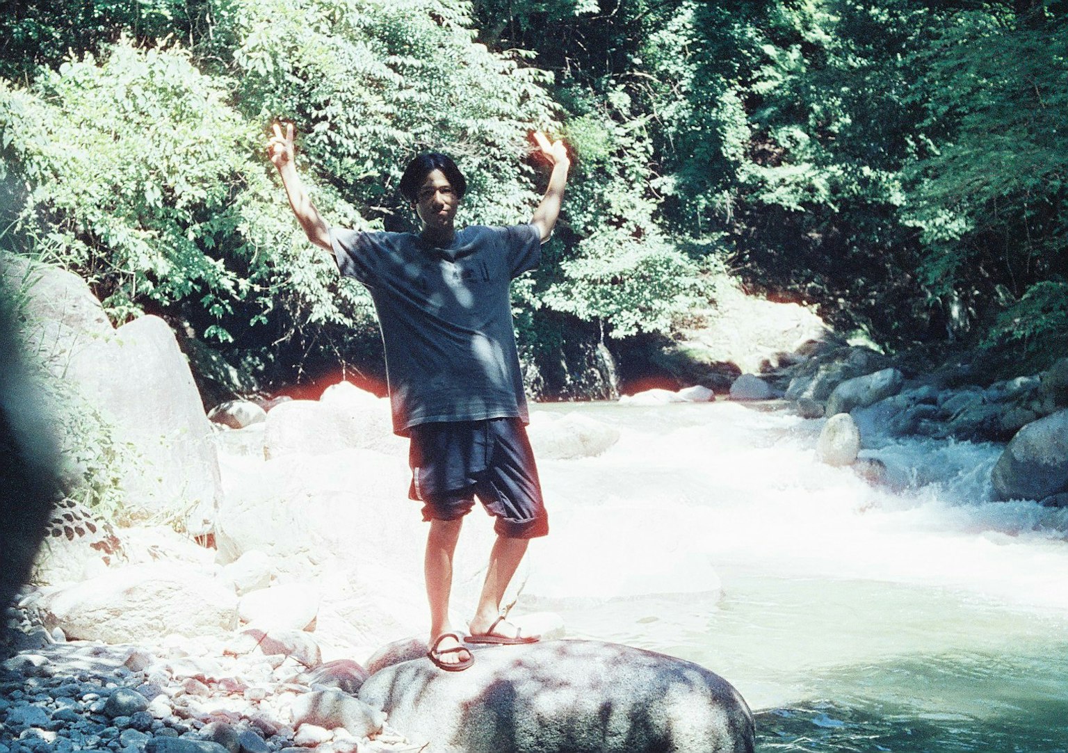 Mann steht auf einem Felsen in einem Fluss umgeben von grünen Bäumen