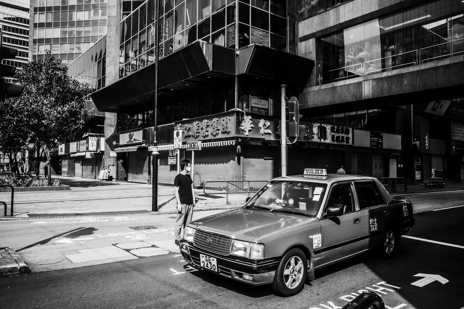 A black and white urban scene featuring a parked taxi and a pedestrian