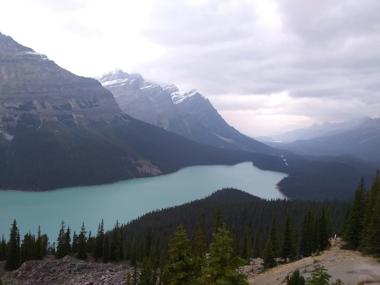 Vista escénica de montañas y un lago con cielos nublados y árboles verdes