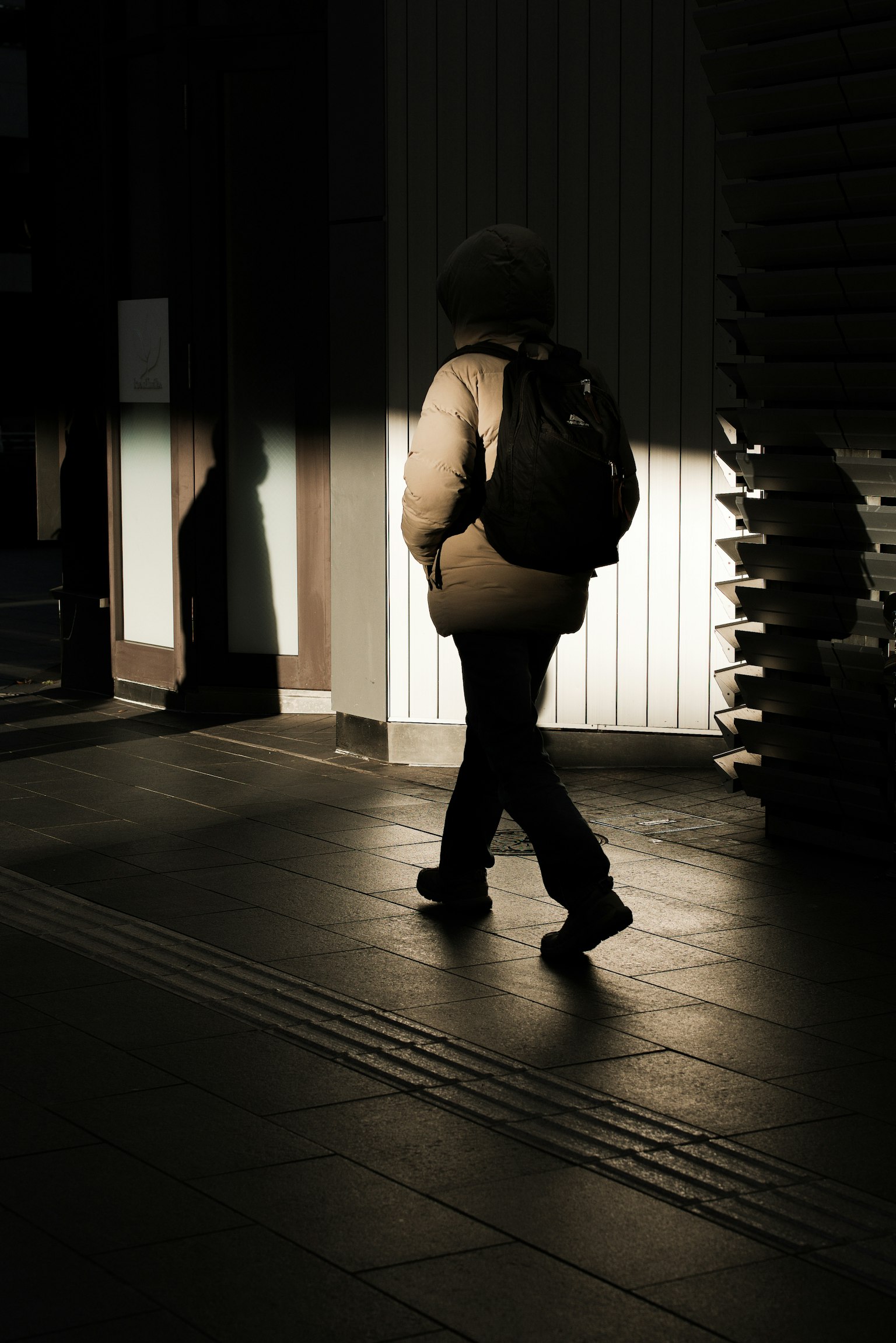 Silueta de una persona caminando con una mochila en un entorno urbano parcialmente iluminado