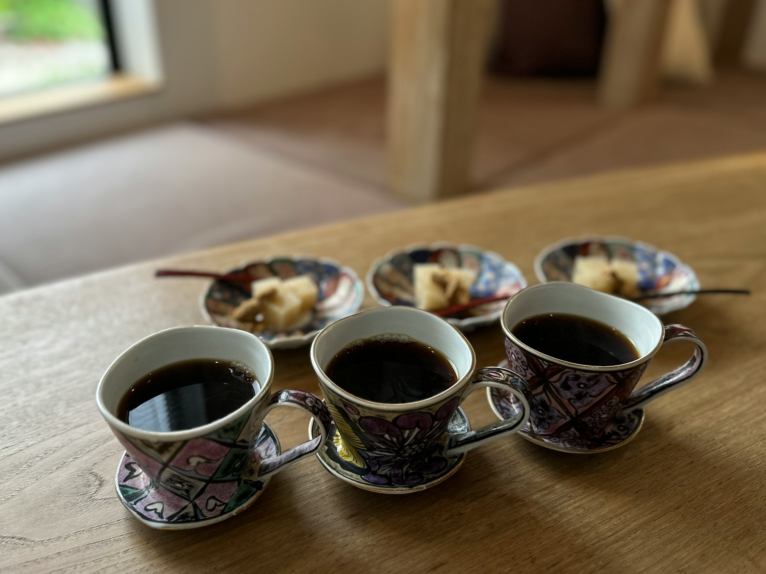 Four ornate coffee cups filled with black coffee on a wooden table with small plates of pastries